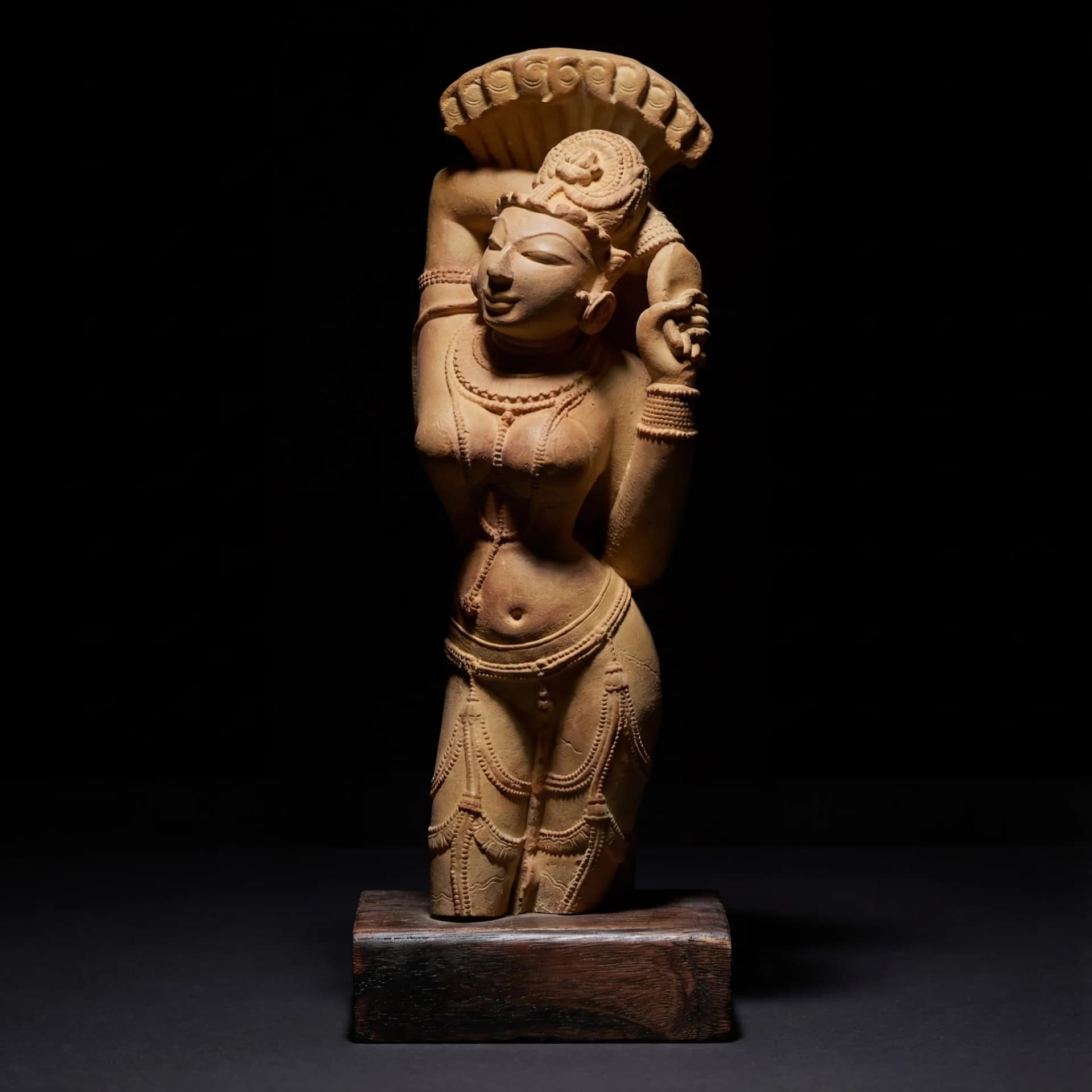 A sandstone Alasa Nayika sculpture standing in a graceful tribhanga pose against a dark, minimalist background.