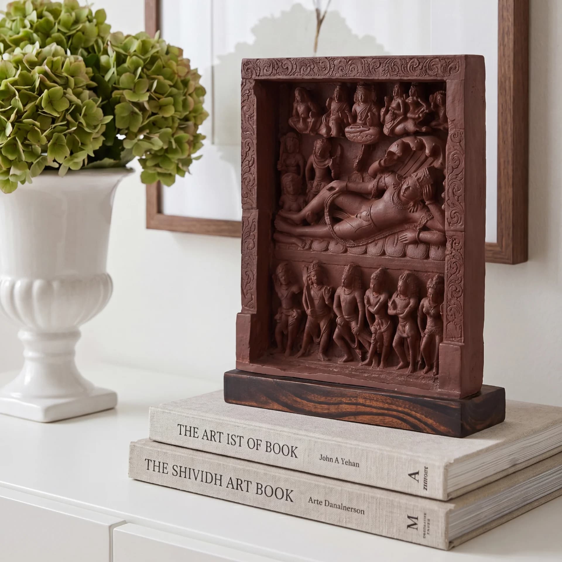 An Anantasayana Vishnu Sculpture museum replica displayed on stacked books, showcasing intricate terracotta-style relief carvings of the reclining deity.