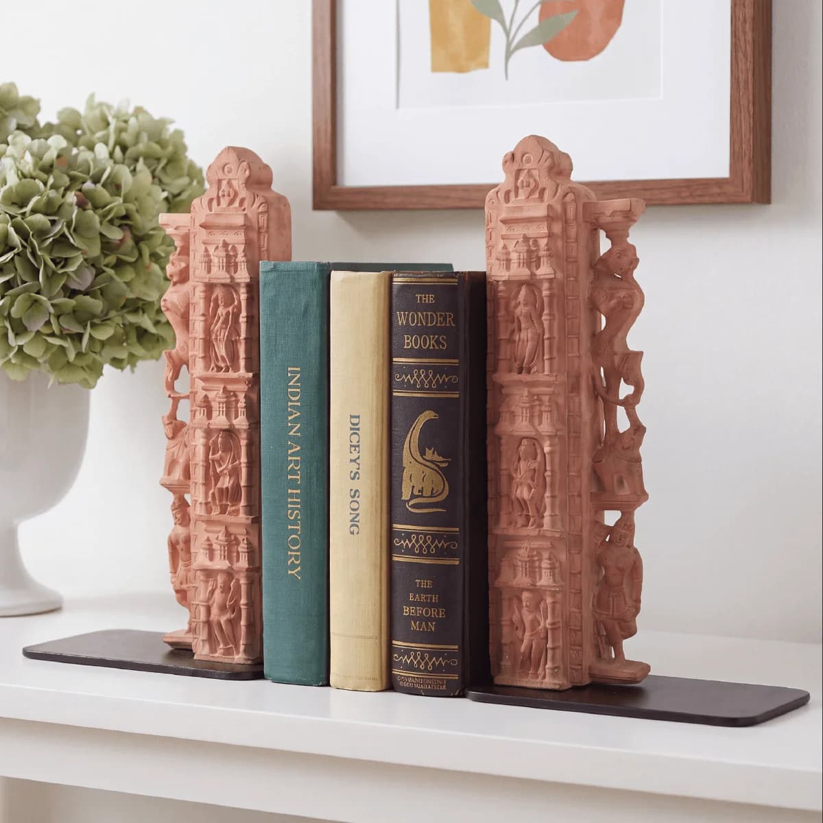 A pair of Dwar Shakha Sculpture bookends crafted from stone composite, holding three vintage books on a white shelf.