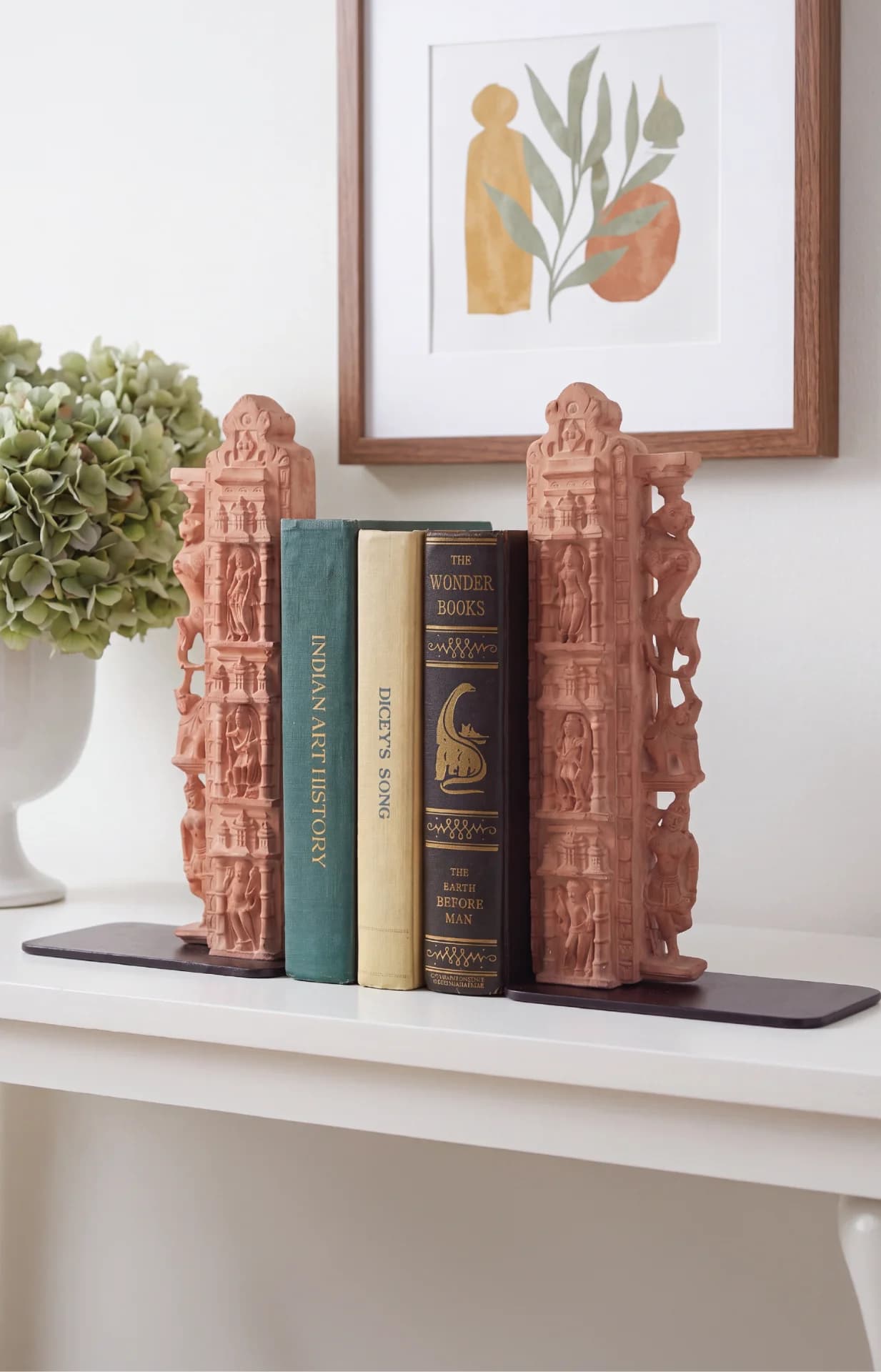 A pair of Dwar Shakha Sculpture bookends crafted from stone composite, holding three vintage books on a white shelf.