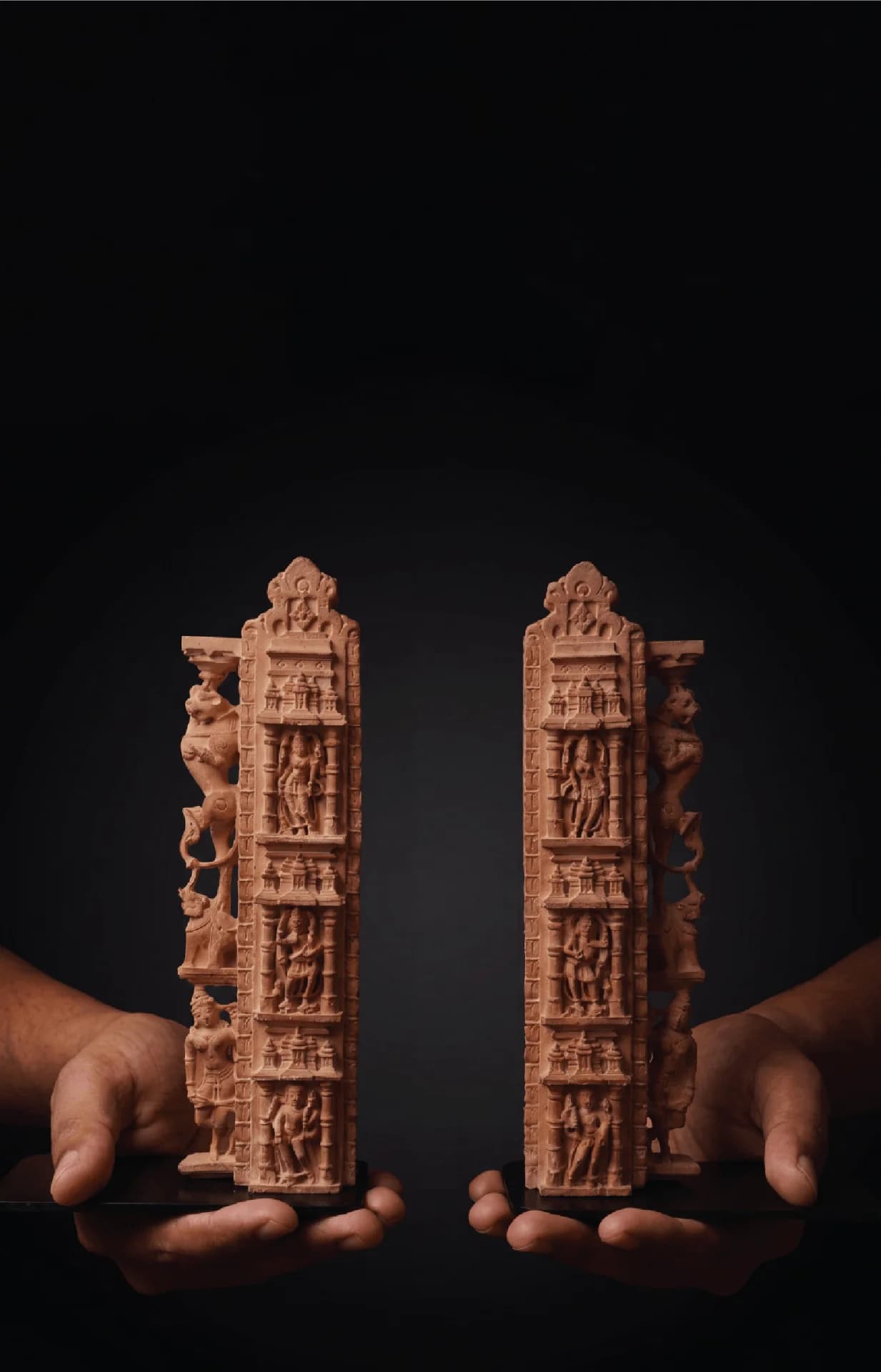 Two hands hold a pair of Dwara Shakha Sculpture bookends, showcasing the intricate stone composite carvings of celestial figures.