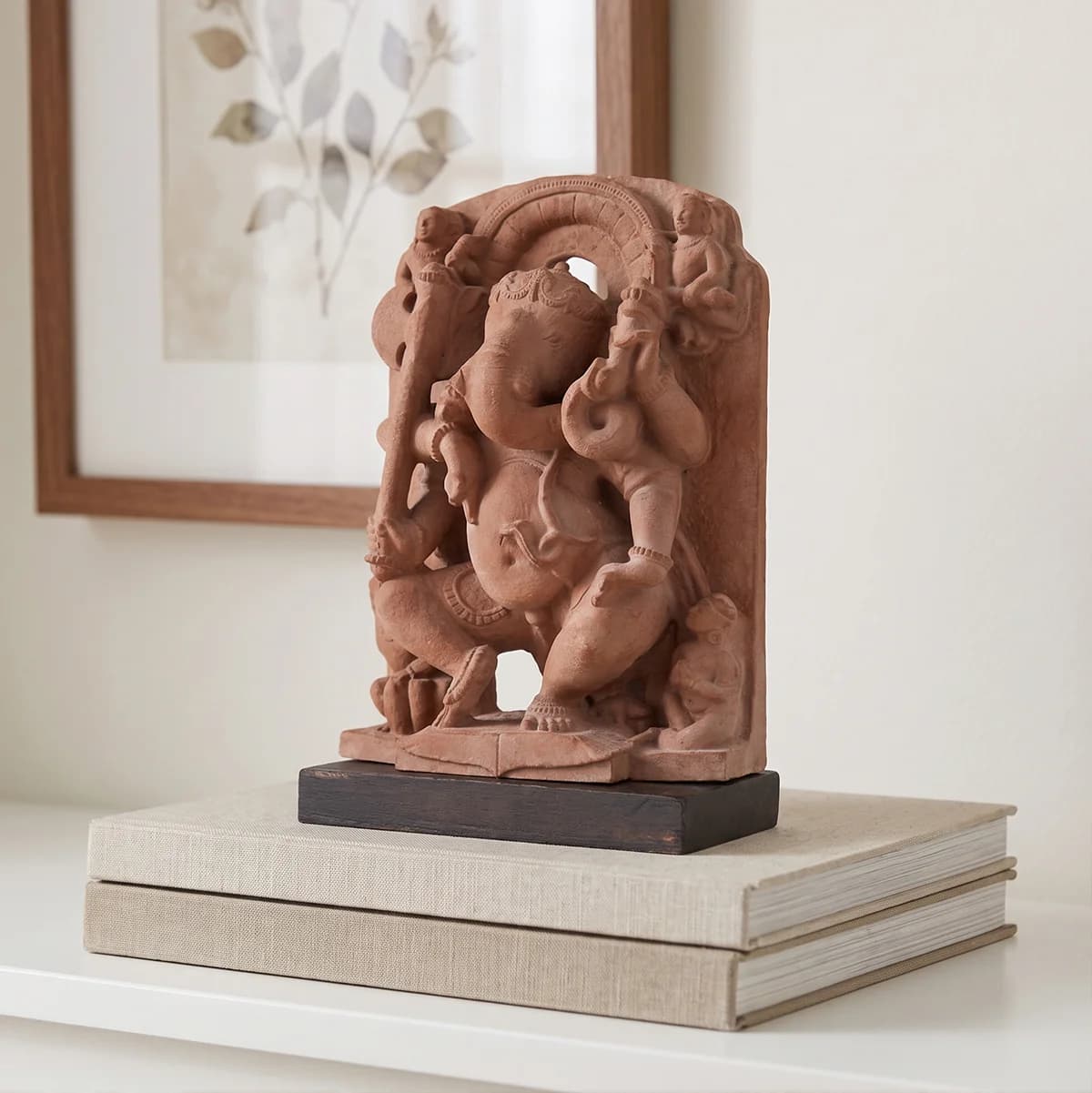 A Ganesha Sculpture museum replica in stone composite, displayed on stacked books, showcasing intricate 10th-century dancing deity iconography.