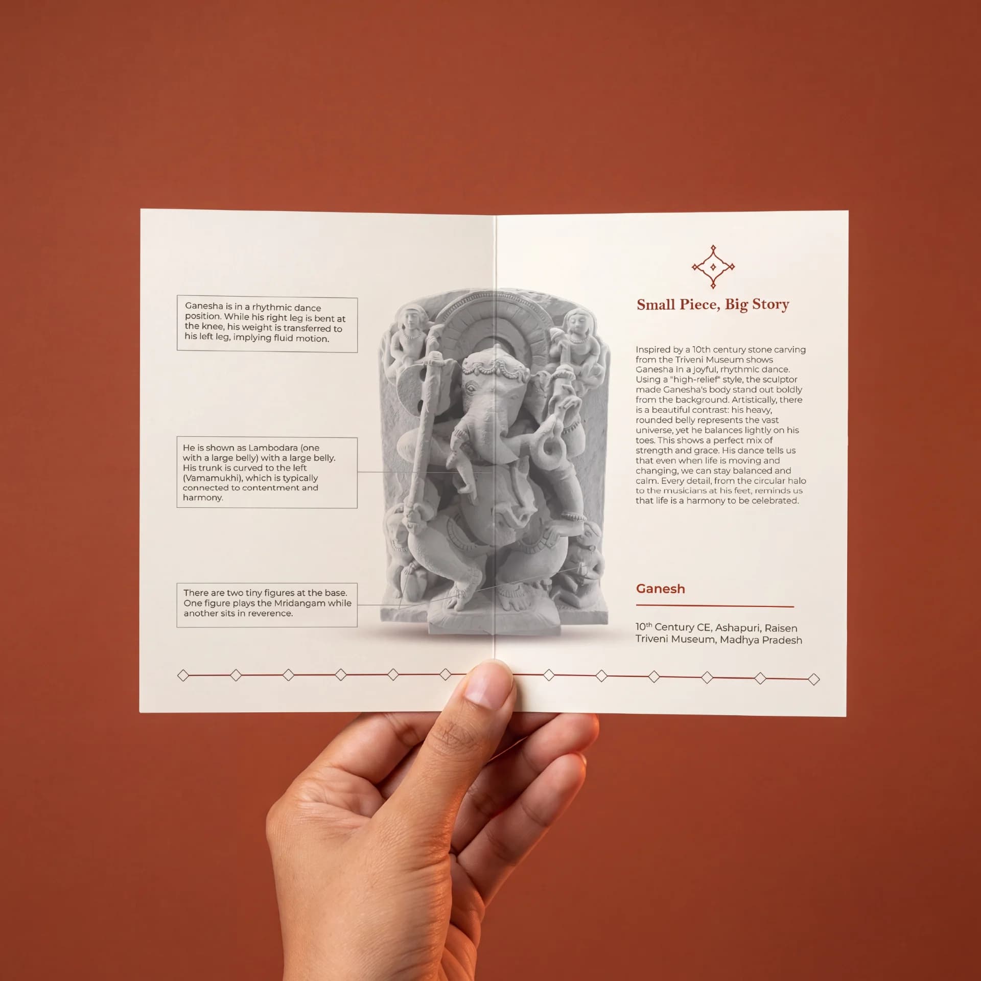 A hand holds an open brochure featuring the Ganesha Sculpture museum replica with detailed annotations about its stone composite craftsmanship.