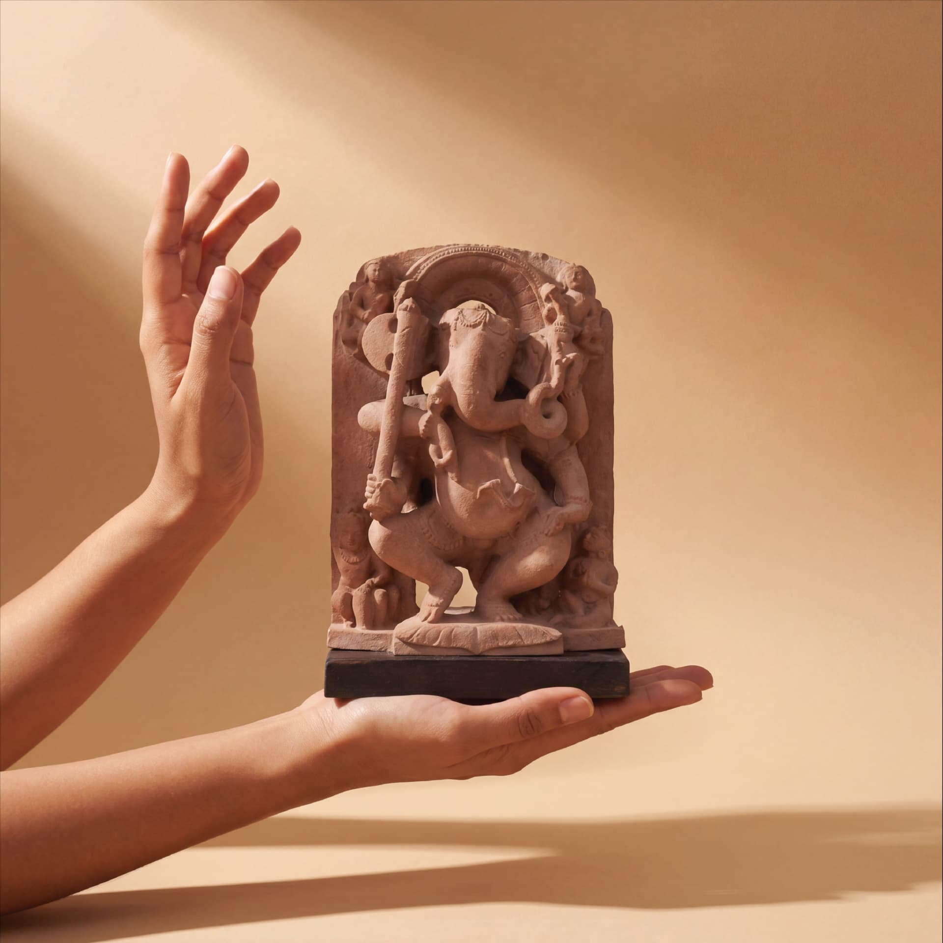 A pair of hands gently cradles a terracotta-style Ganesha Sculpture, showcasing the intricate 10th-century temple art replica details.