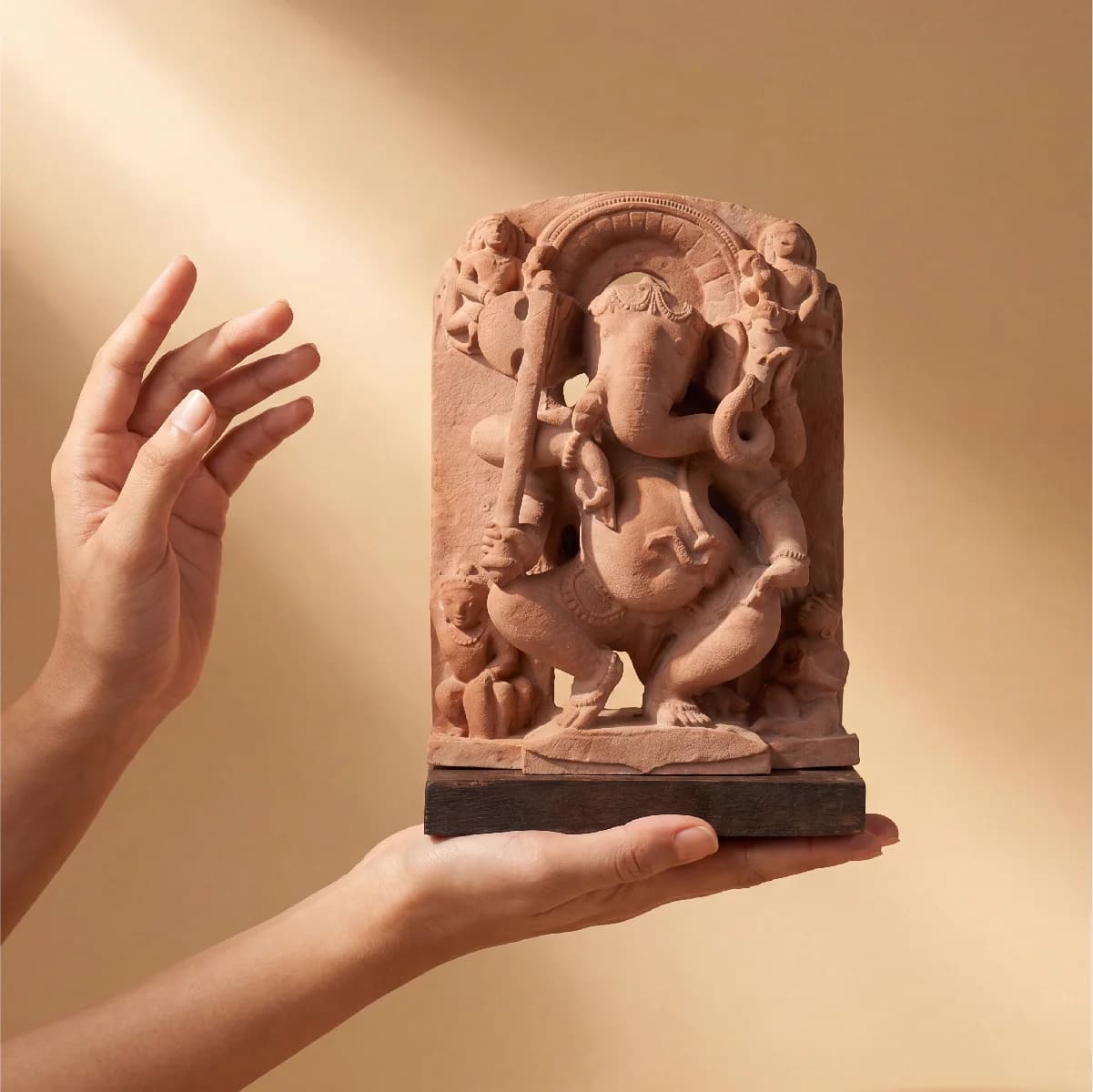 A pair of hands gently cradles a stone composite Ganesha Sculpture, showcasing the intricate 10th-century temple art replica details.