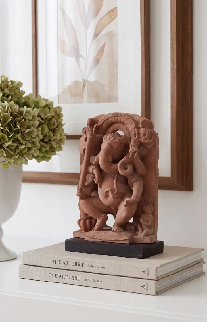 A Ganesha Sculpture museum replica in stone composite displayed on books, showcasing intricate dancing deity details in a home setting.