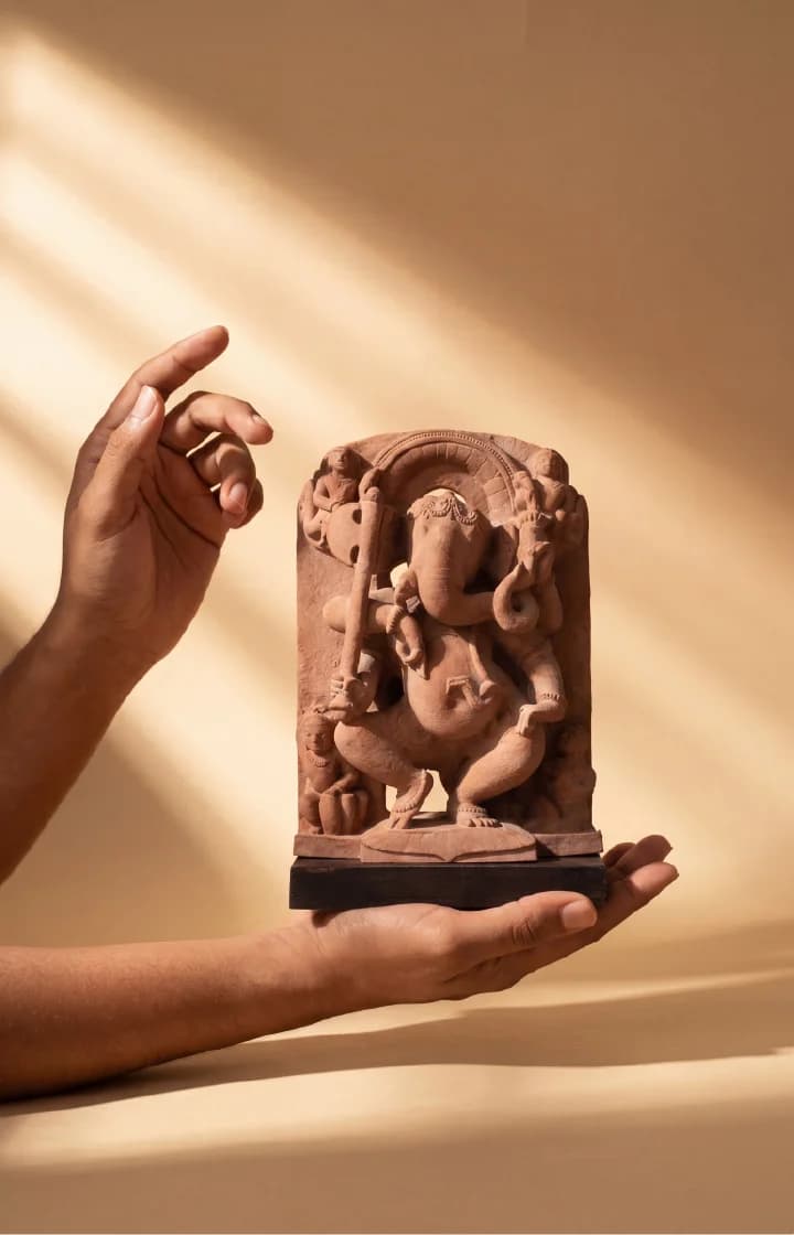 A pair of hands holds a hand-finished stone composite Ganesha Sculpture, showcasing the intricate details of the dancing deity.