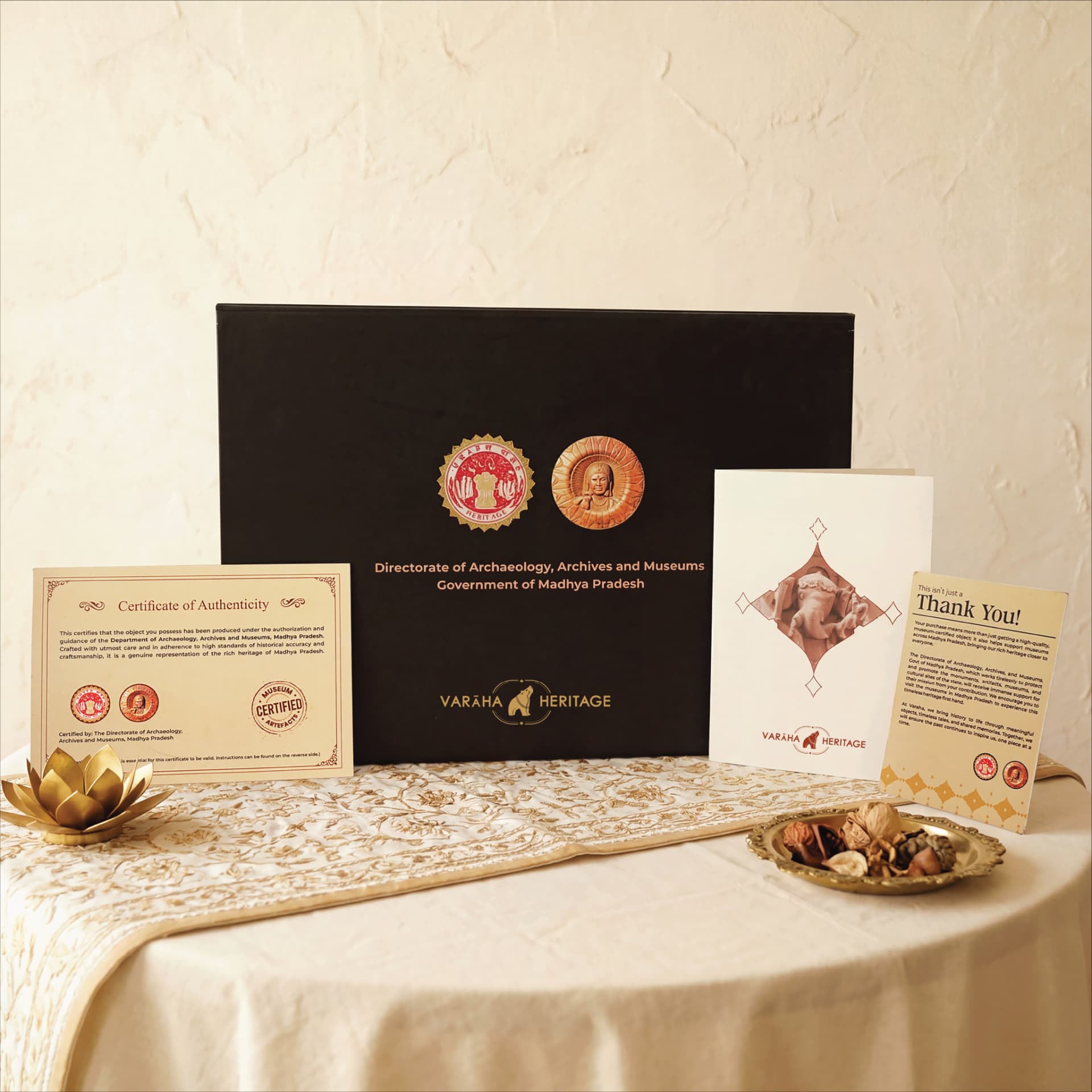 A Ganesha Sculpture packaging set featuring a black gift box, certificate of authenticity, and thank you card on a table.