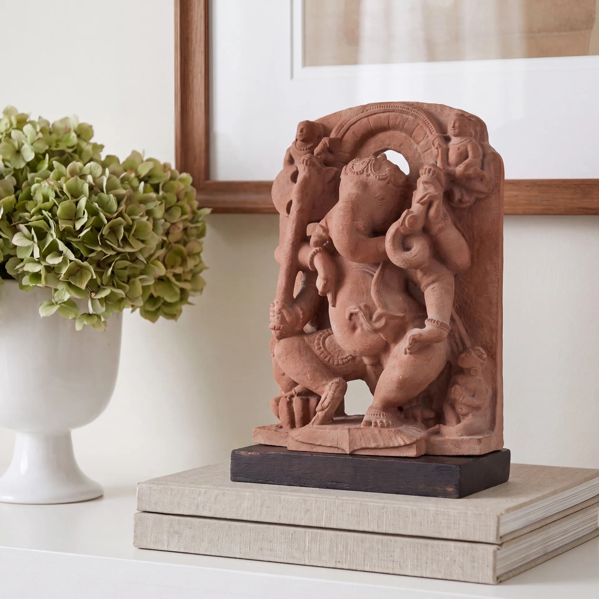 A stone composite Ganesha Sculpture replica displayed on stacked books next to a vase of green hydrangeas.