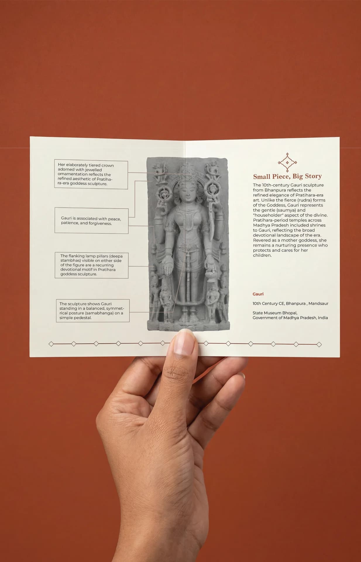 A hand holds an informational brochure featuring the Gauri Parvati Sculpture, a stone composite replica of Pratihara temple art.