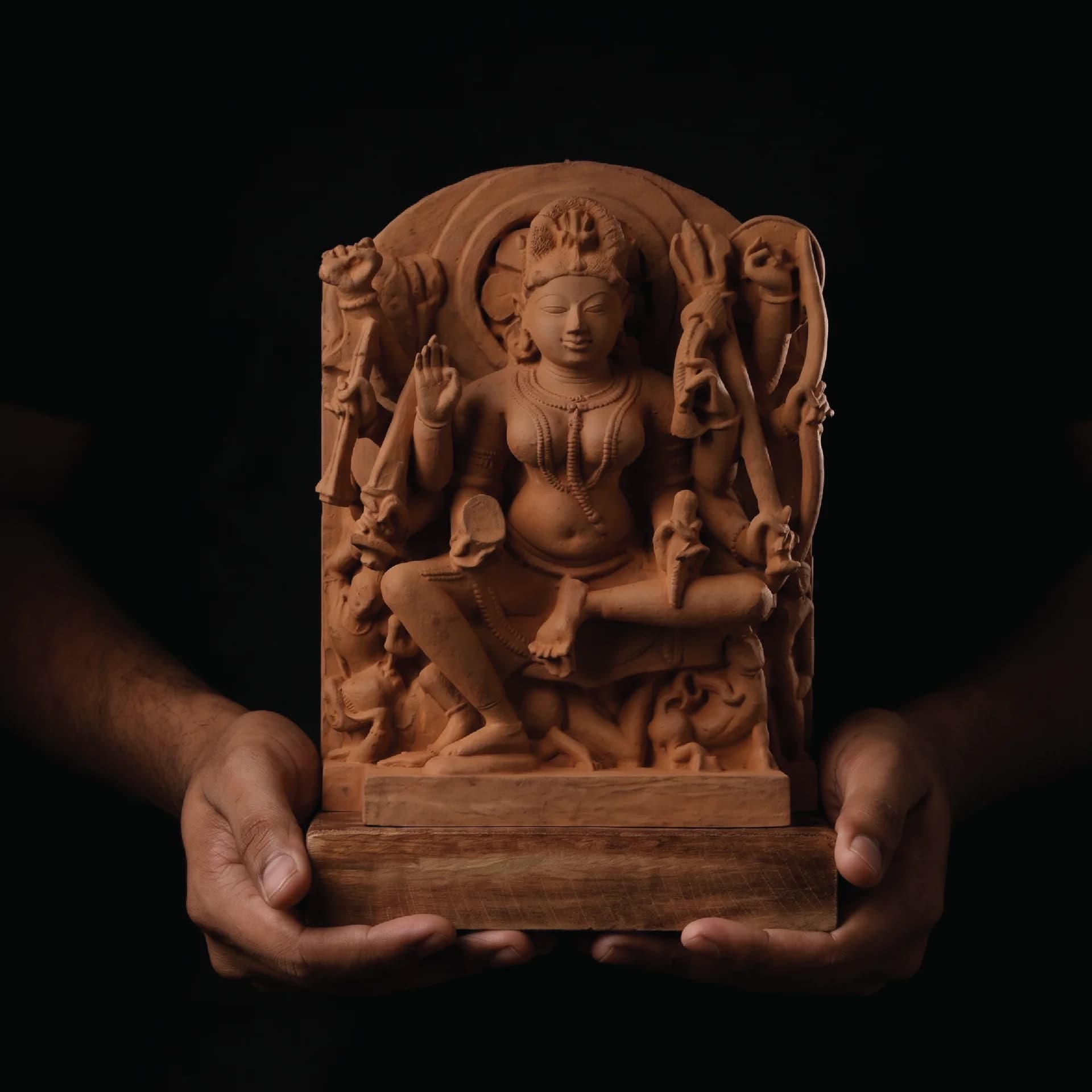 A pair of hands holds a hand-finished stone Goddess Durga Sculpture, showcasing the intricate medieval-style carved relief details.
