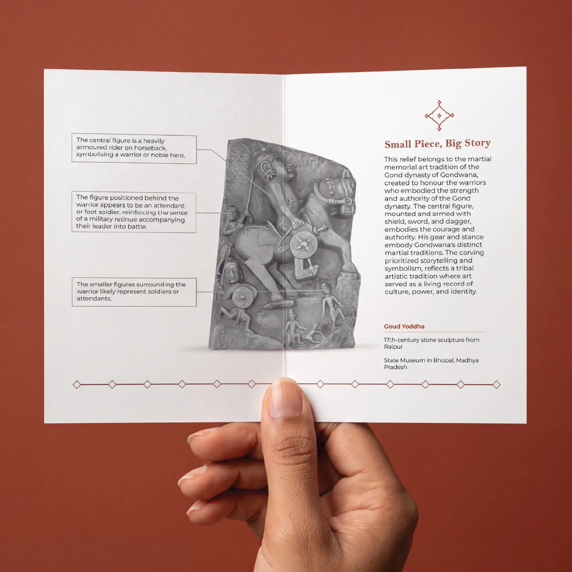 A hand holds an informational brochure featuring the Goud Yoddha stone sculpture with detailed annotations about the warrior relief.