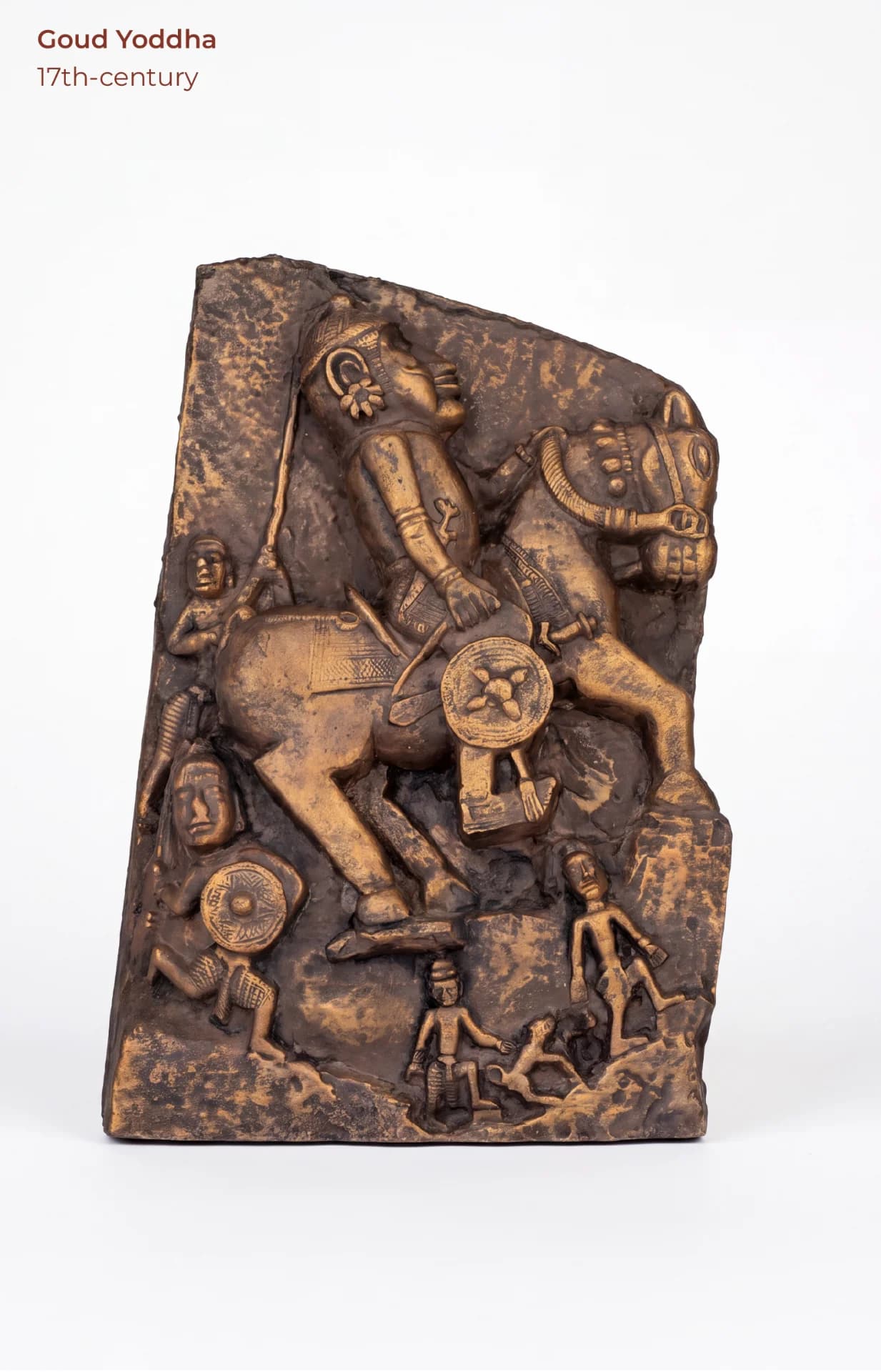 A bronze-toned Goud Yoddha replica featuring a detailed stone-carved relief of a mounted warrior surrounded by smaller figures.