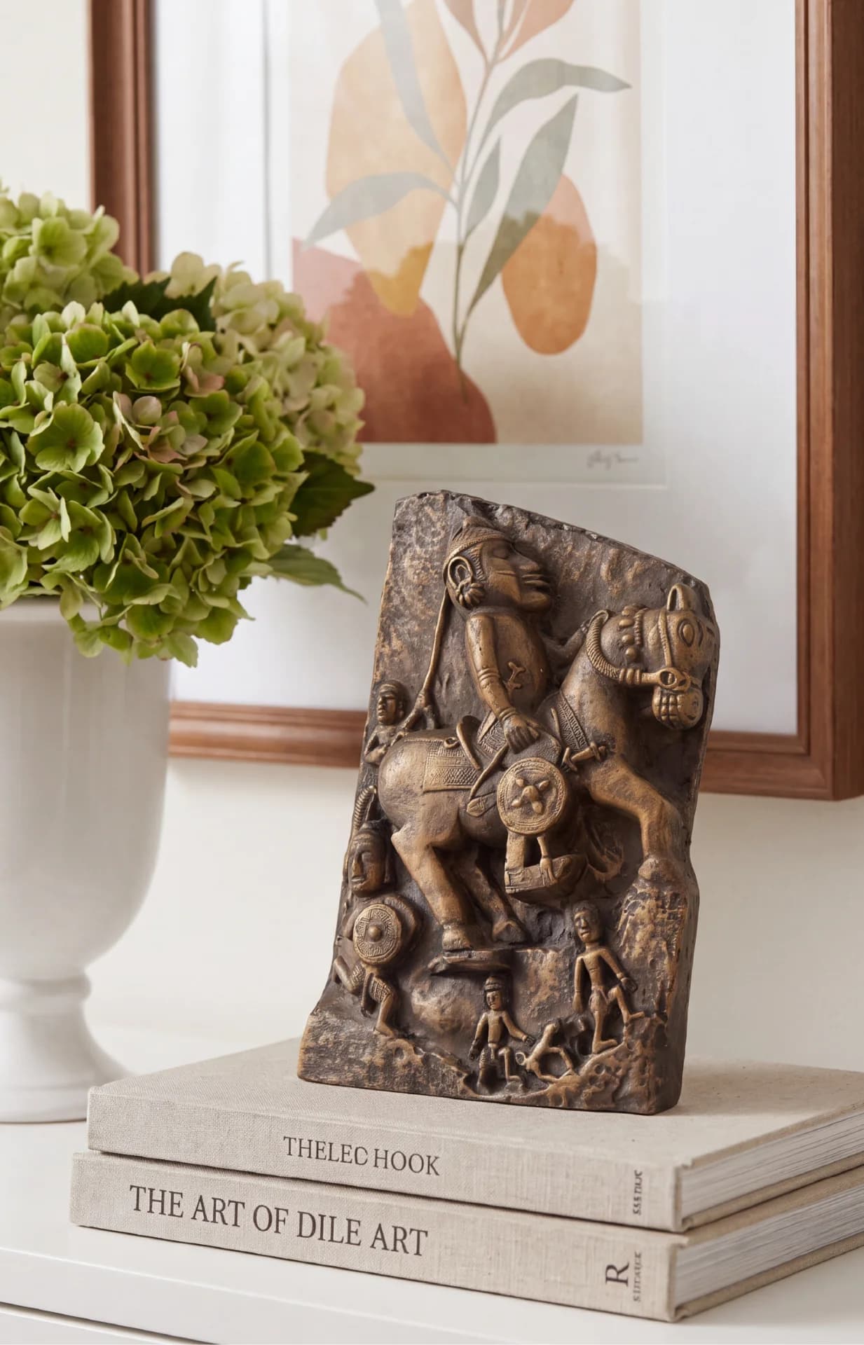 The Goud Yoddha stone-finish sculpture displayed on stacked books, featuring a detailed relief of a mounted Gond warrior.