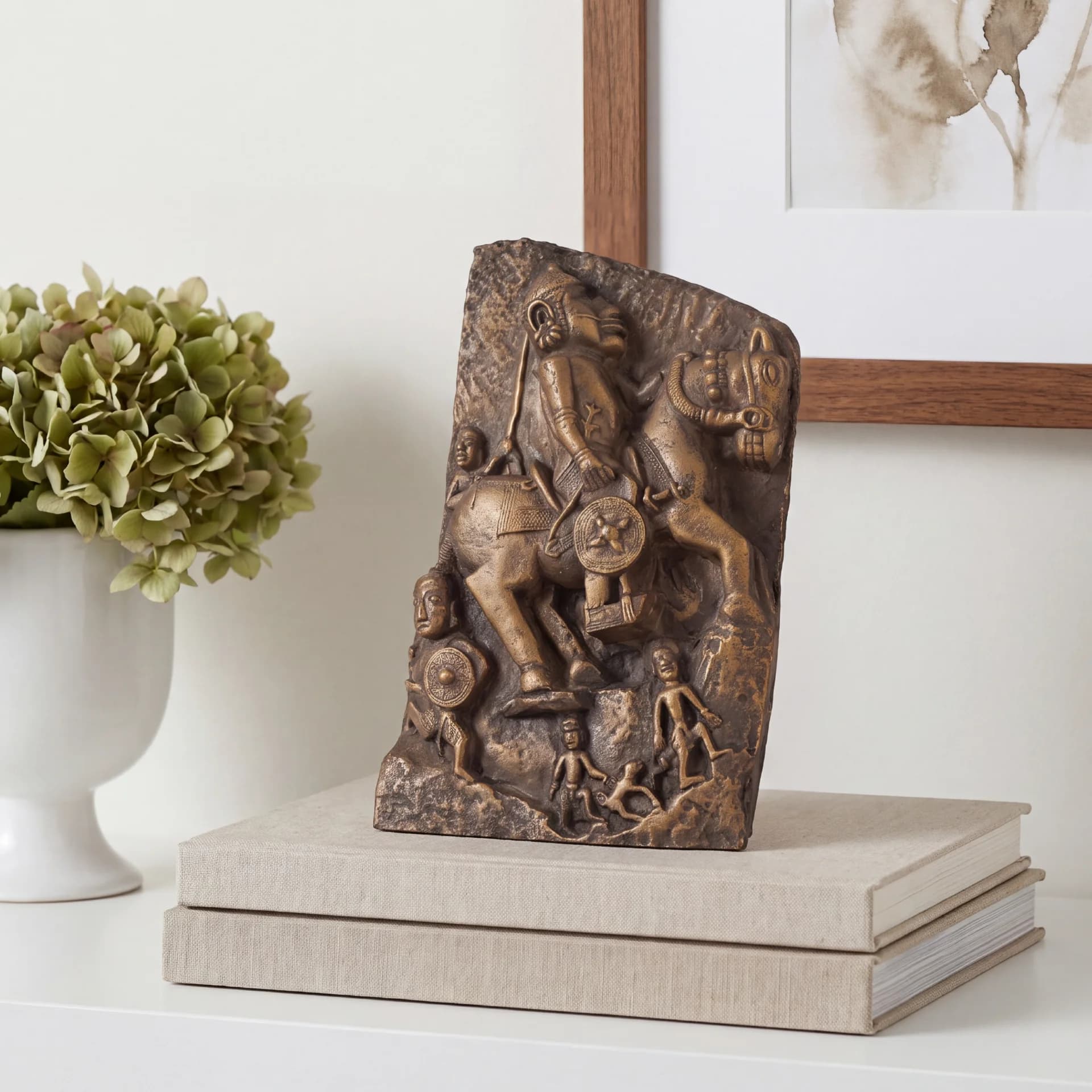 The Goud Yoddha stone-effect sculpture sits on stacked books, showcasing a detailed relief of a warrior on horseback.