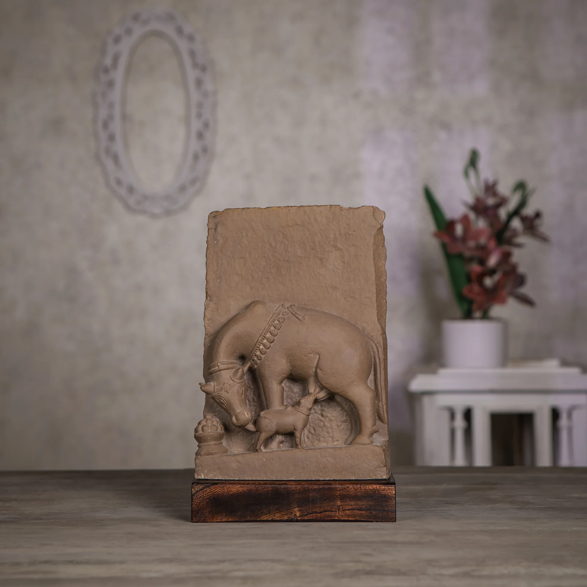 A stone composite Kamdhenu Sculpture replica showing a cow nursing its calf, displayed on a wooden base.