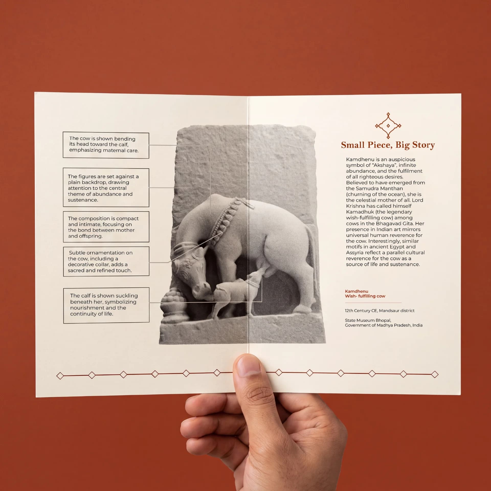 A hand holds an informational brochure featuring the Kamdhenu Sculpture, a stone composite museum replica of a divine cow.