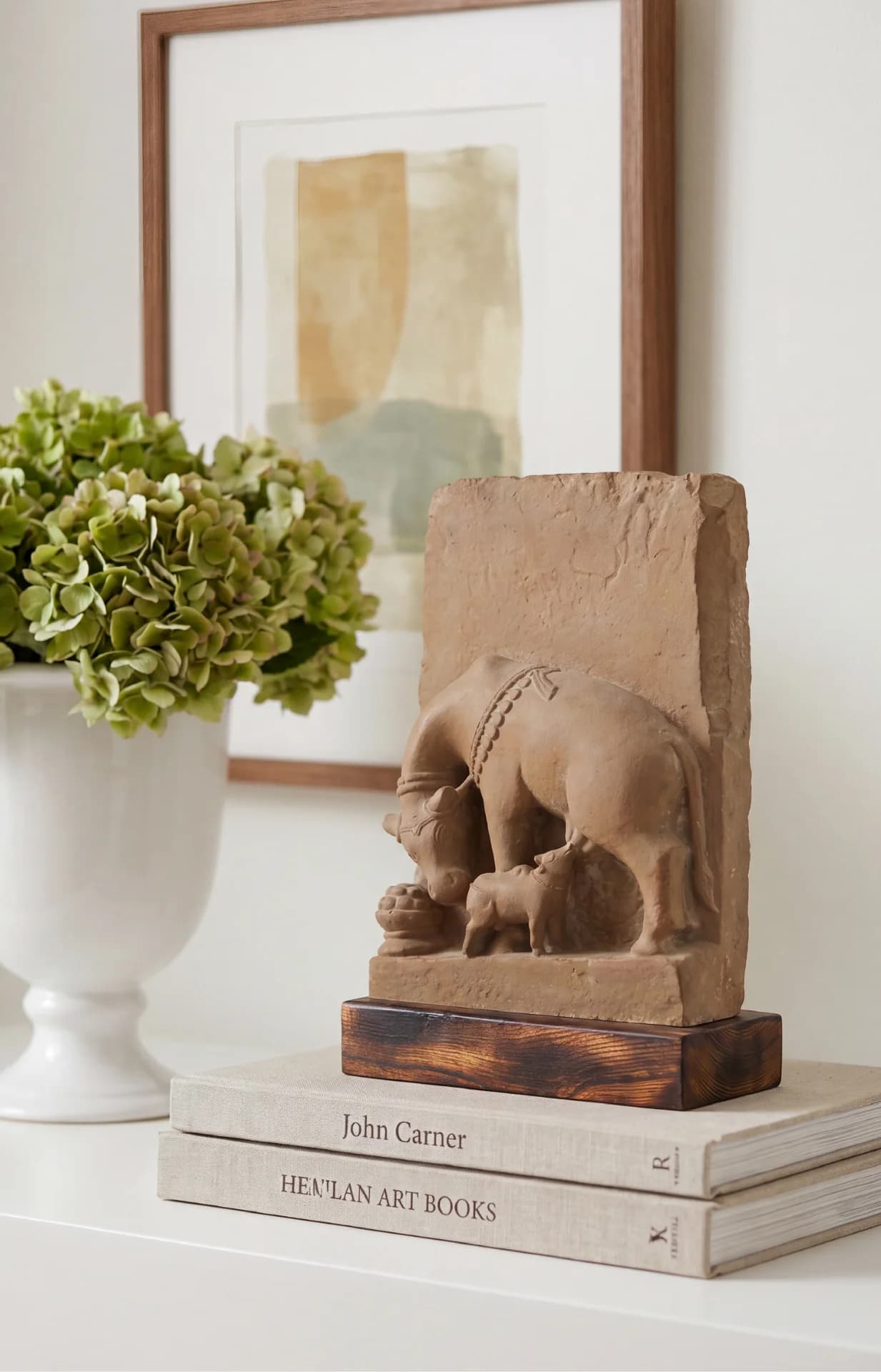 The Kamdhenu Sculpture museum replica, a stone composite artifact, displayed on a stack of books next to a floral arrangement.