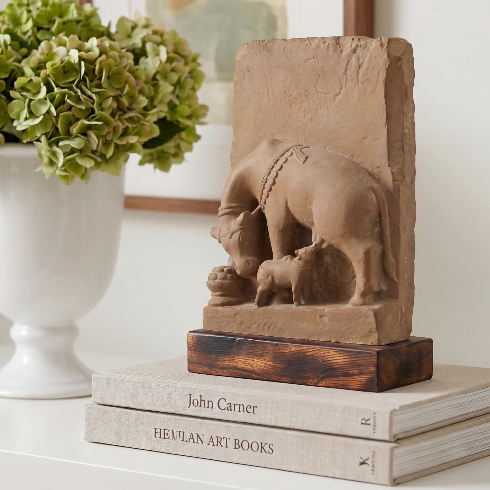 A stone composite Kamdhenu Sculpture resting on a stack of books, featuring the divine cow nursing her calf.