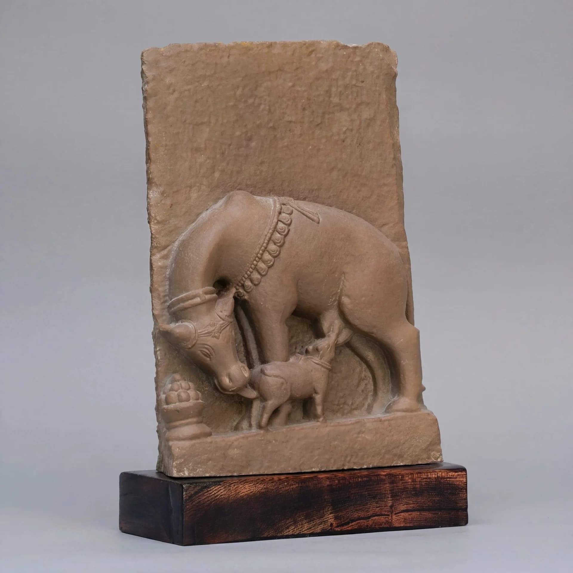 A stone composite Kamdhenu sculpture showing a mother cow nursing her calf, mounted on a sturdy wooden base.