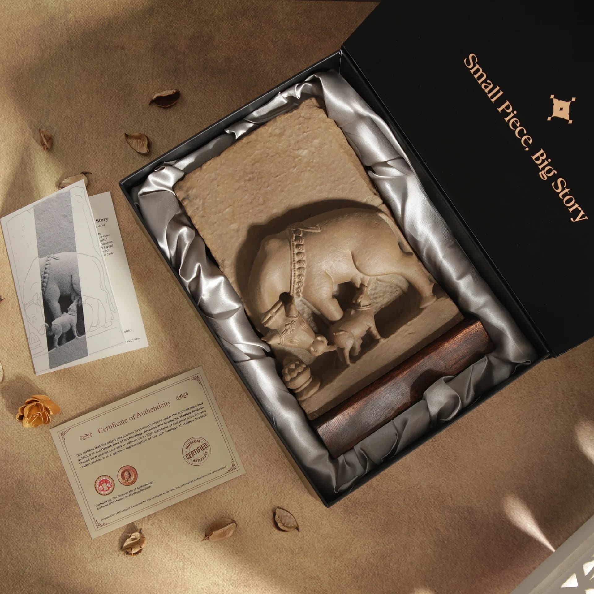 A stone composite Kamdhenu Sculpture displayed inside a premium gift box with its certificate of authenticity and story card.