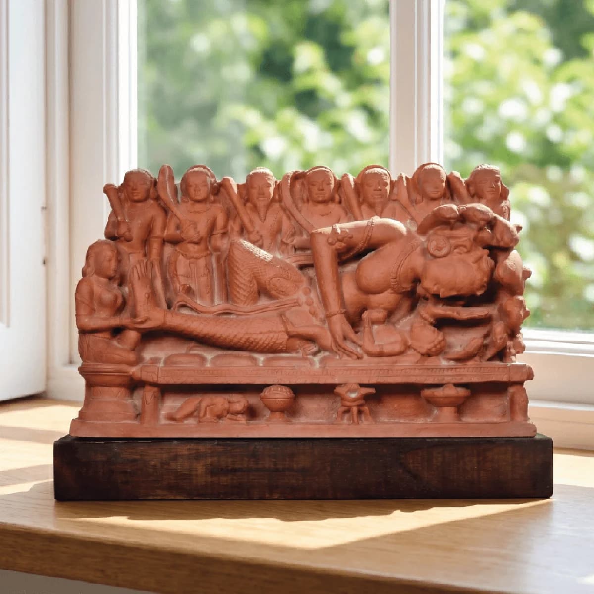 A terracotta-style Krishna's Birth Sculpture replica featuring Devaki and attendants, displayed on a wooden base near a window.
