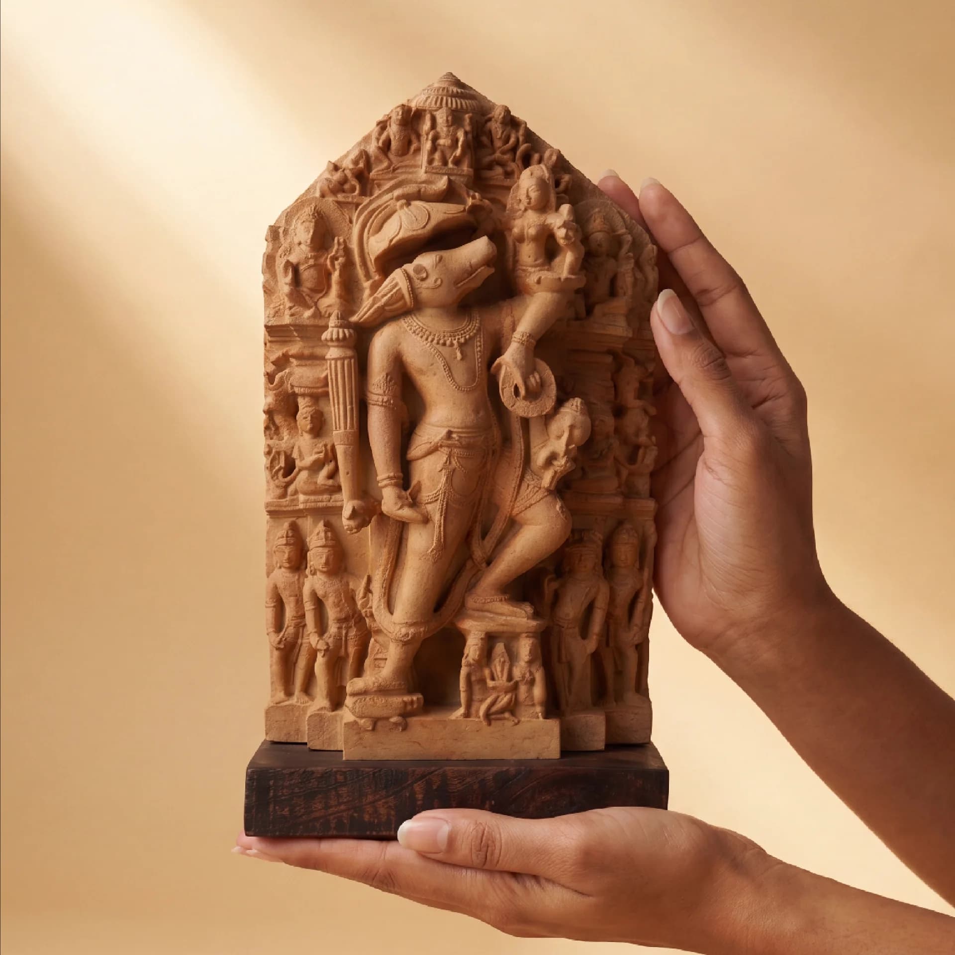 Hands hold a stone composite Nar Varaha Sculpture, showcasing the intricate man-boar Vishnu avatar relief against a neutral background.