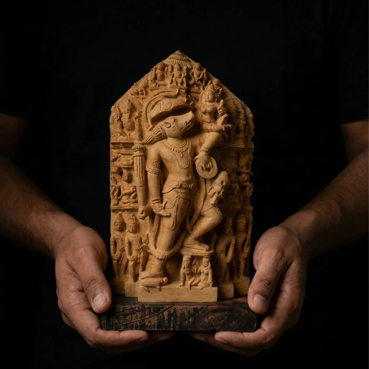 A pair of hands holds a detailed Nar Varaha Sculpture, a stone composite replica featuring intricate temple art carvings.