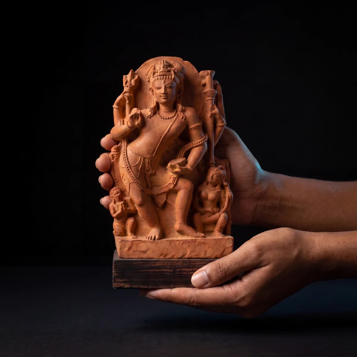 A pair of hands holds a hand-finished stone composite Natesh Shiva Sculpture against a dark, minimalist background.