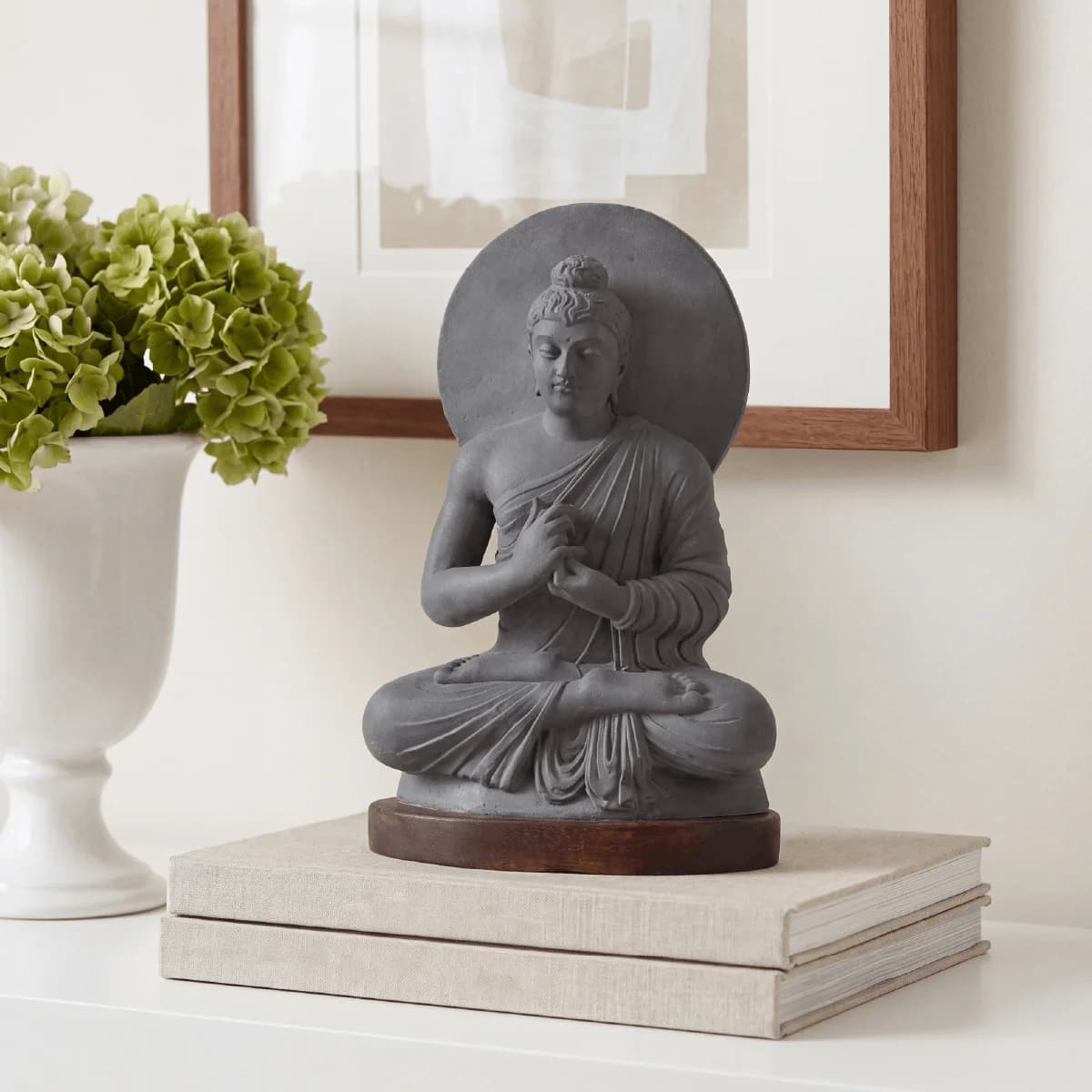A stone composite Preaching Buddha statue sits on stacked books, showcasing the serene Gandhara art tradition in a home setting.