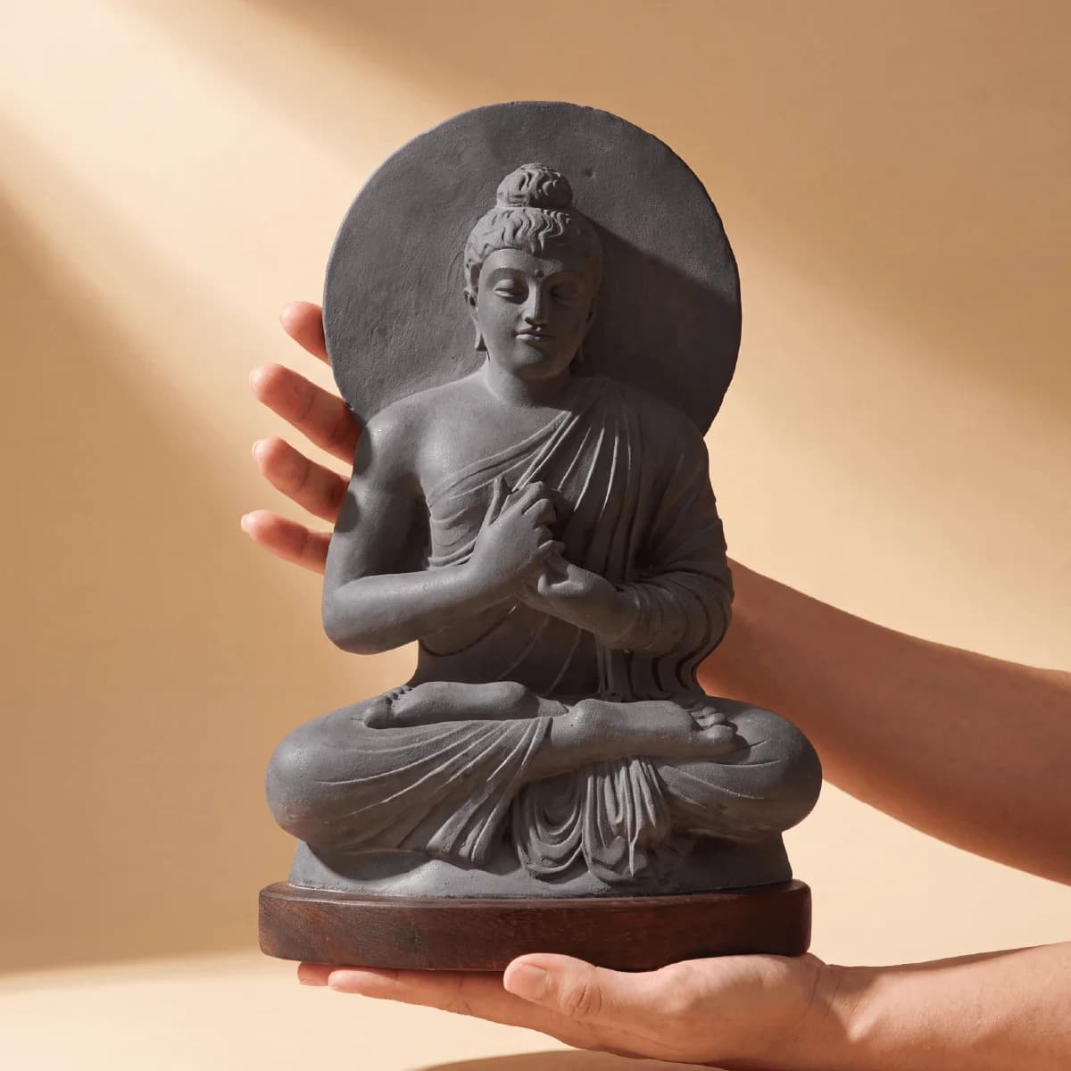 A pair of hands holds a dark stone composite Preaching Buddha statue, showcasing the intricate Gandhara style craftsmanship.
