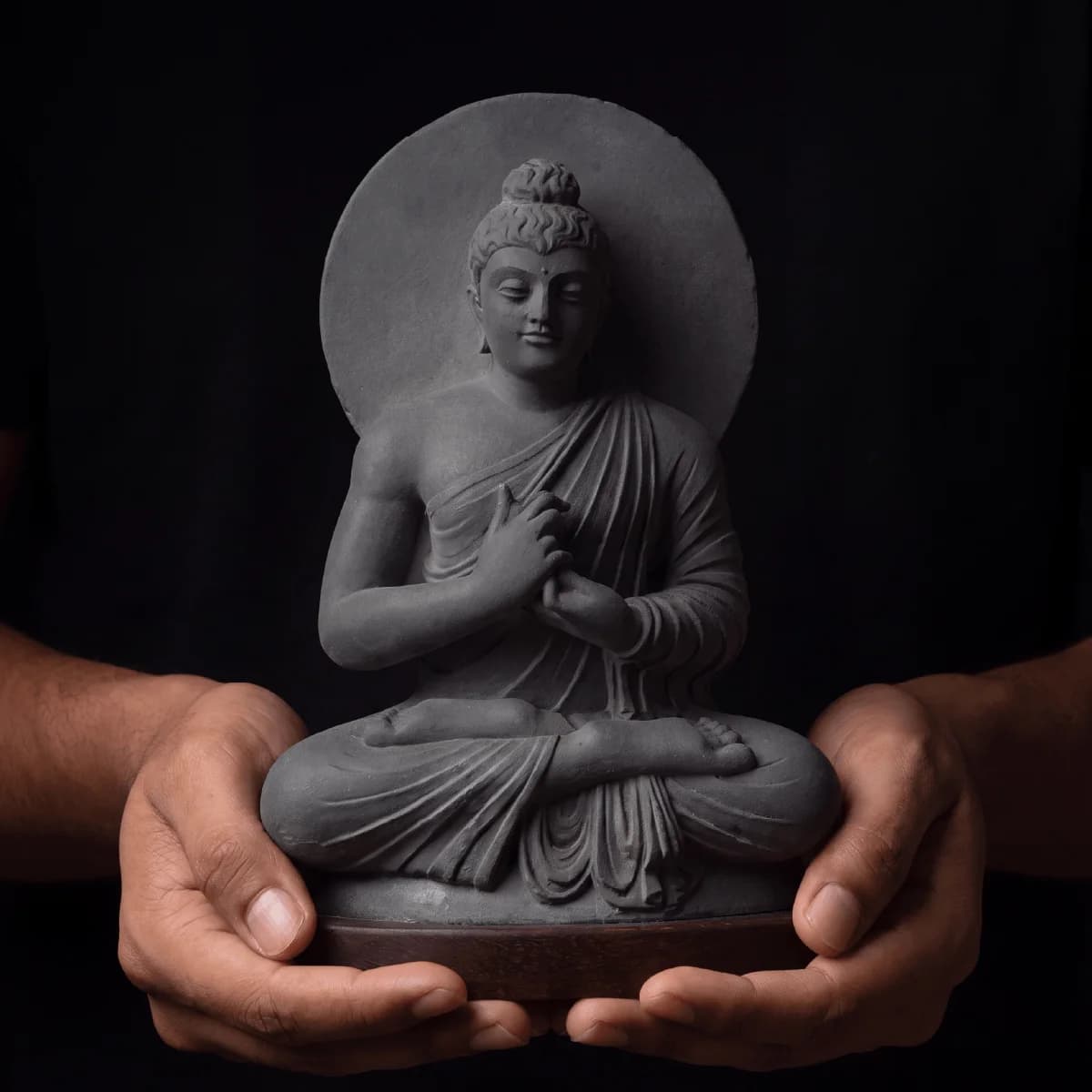 Close-up of hands holding a stone composite Preaching Buddha statue, showcasing the intricate Gandhara style seated figure.