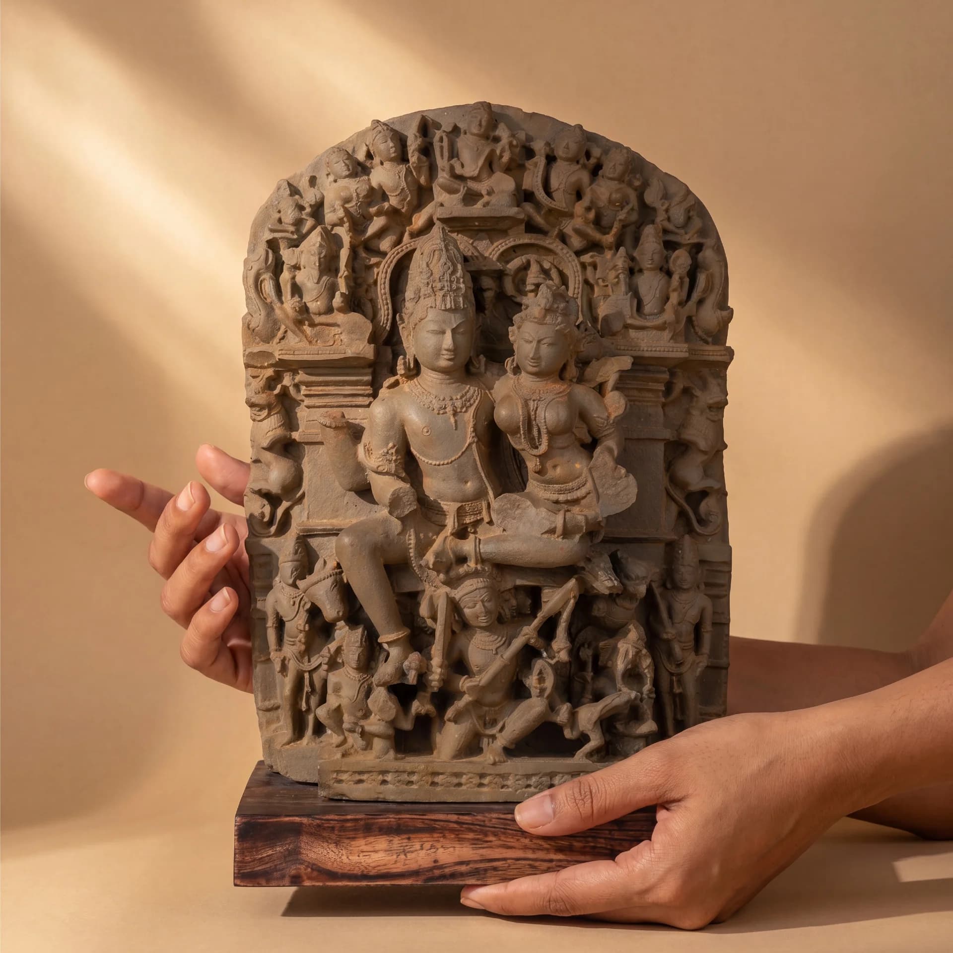 Hands hold a stone composite Ravananugraha Sculpture, showcasing the intricate 11th-century temple art relief against a neutral background.