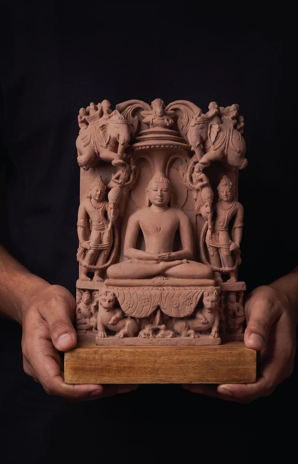 A person holds a stone composite Adinath Sculpture, featuring intricate carvings of the Tirthankara seated in a meditative posture.