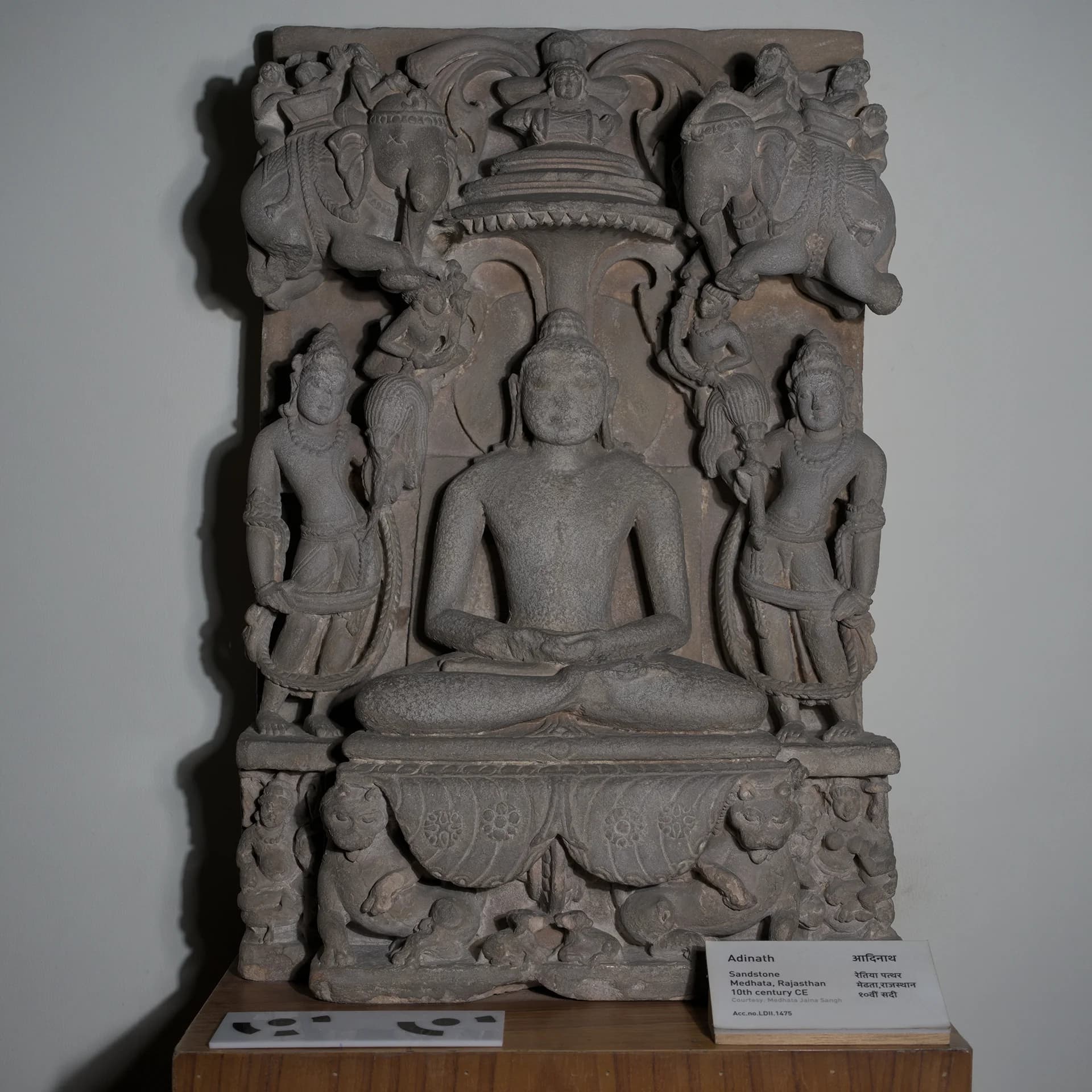 A front-facing view of the Adinath Sculpture, a stone composite museum replica featuring intricate carvings of a seated Tirthankara.