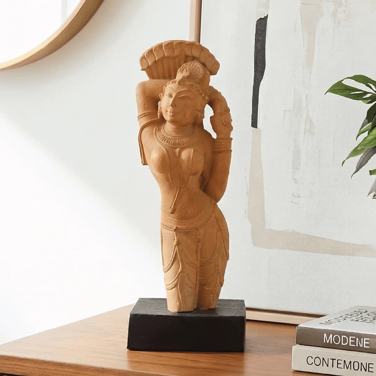 The Alasa Nayika sculpture in a stone composite finish, standing gracefully on a dark wooden base in a home setting.