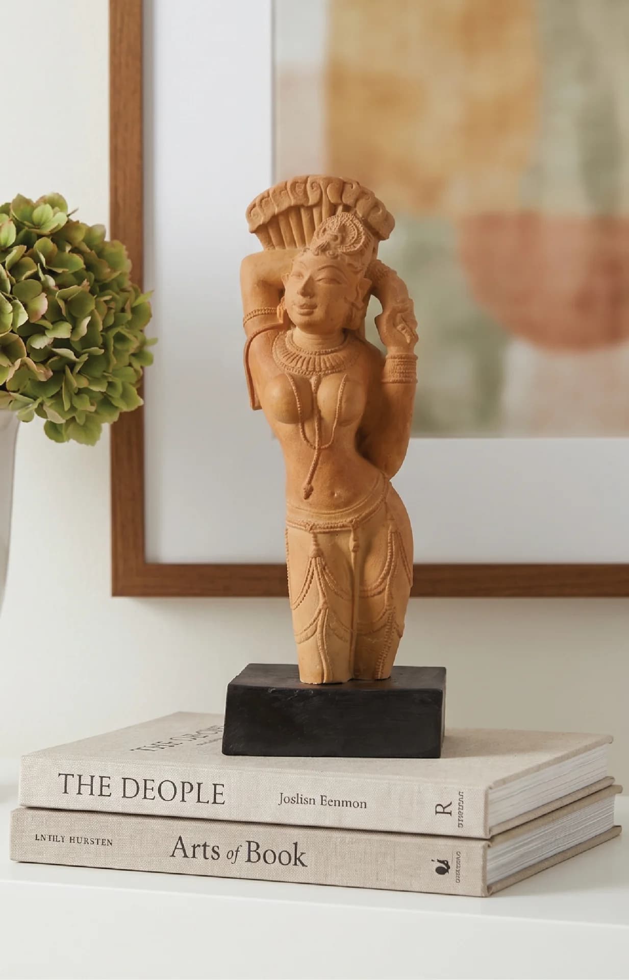 The Alasa Nayika Sculpture, a stone composite replica, stands elegantly on a stack of books in a home setting.