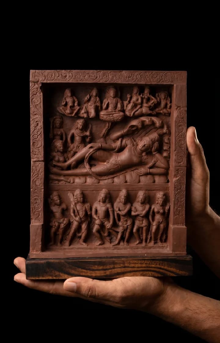 Hands hold an Anantasayana Vishnu Sculpture, a terracotta-style replica featuring intricate Gupta-period relief carvings of deities on a dark background.