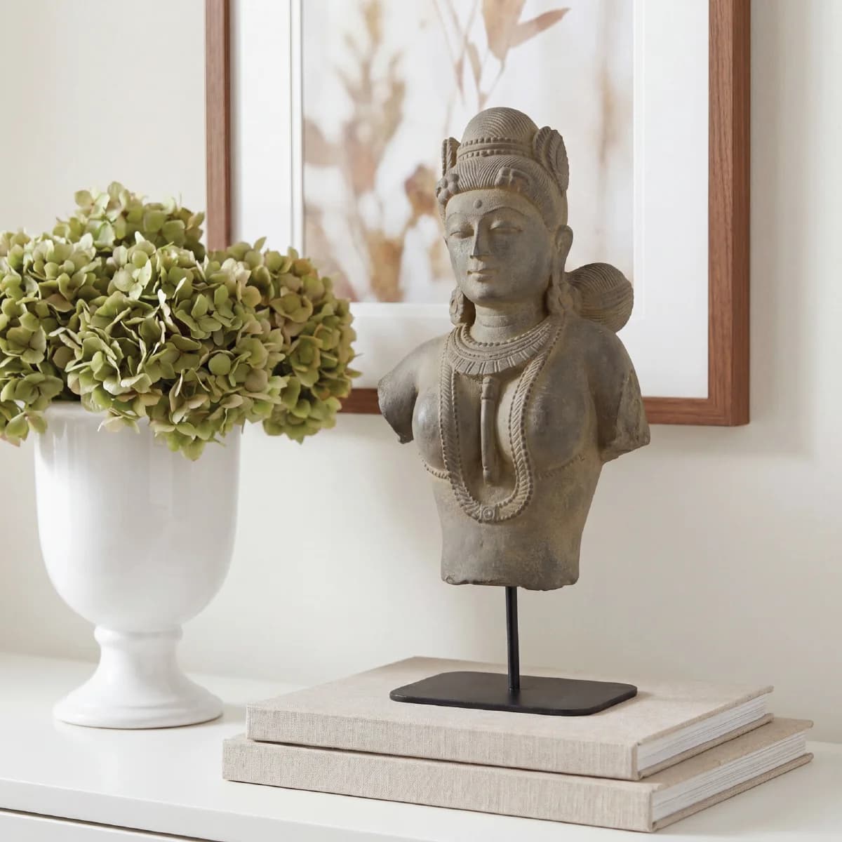 A Female Figure Bust Sculpture displayed on books next to a white vase, featuring detailed stone composite craftsmanship.