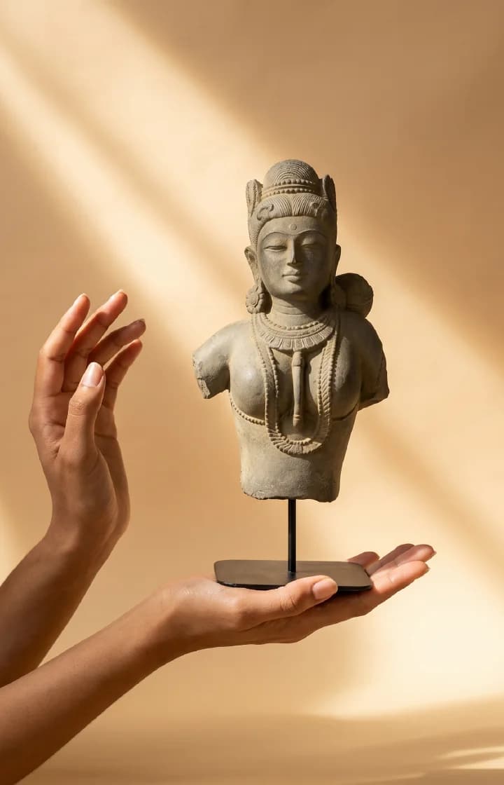 A pair of hands holds a Female Figure Bust Sculpture, a stone composite replica featuring intricate Chola-style jewelry and details.