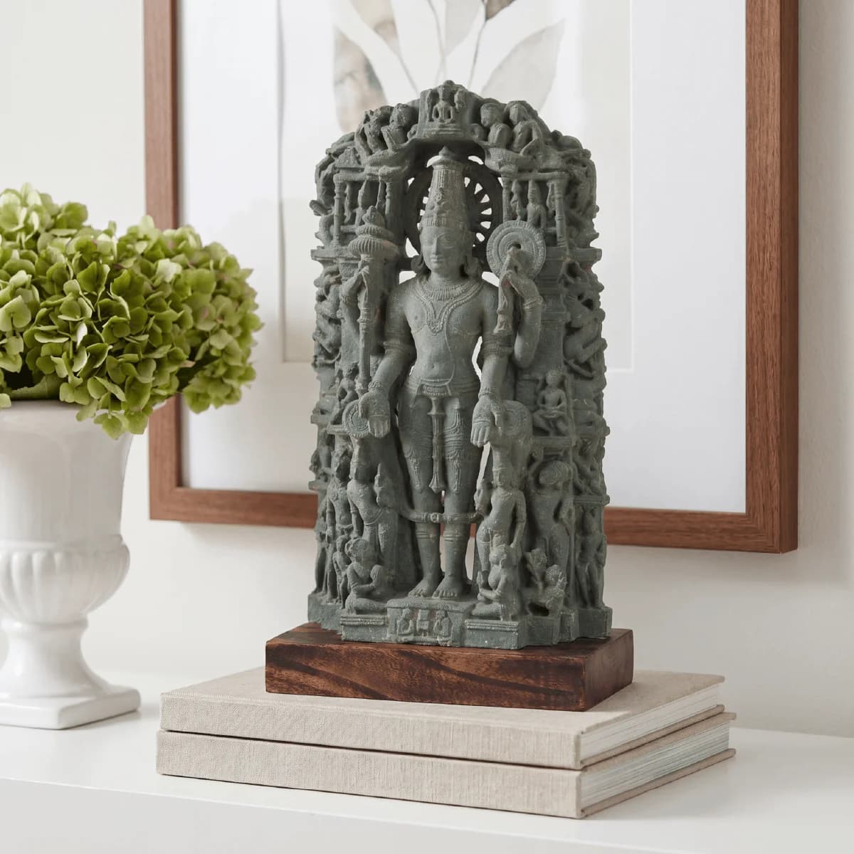 The Chaturbhuj Vishnu Sculpture, a hand-finished stone composite replica, stands elegantly on a stack of books against a white wall.