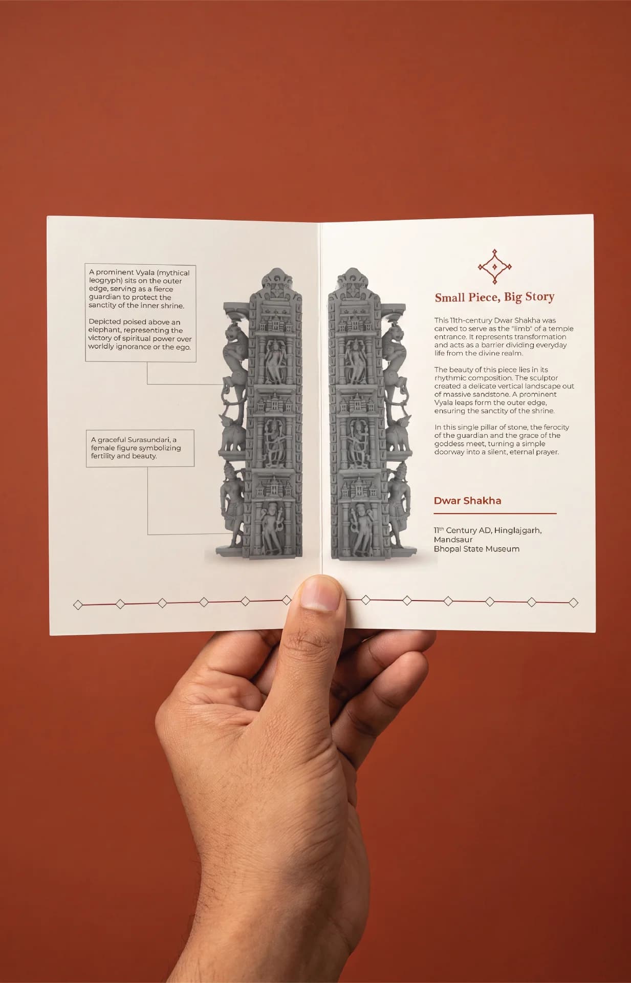 A hand holds an open brochure featuring the Dwara Shakha Sculpture, showcasing detailed stone composite carvings of celestial figures and guardians.