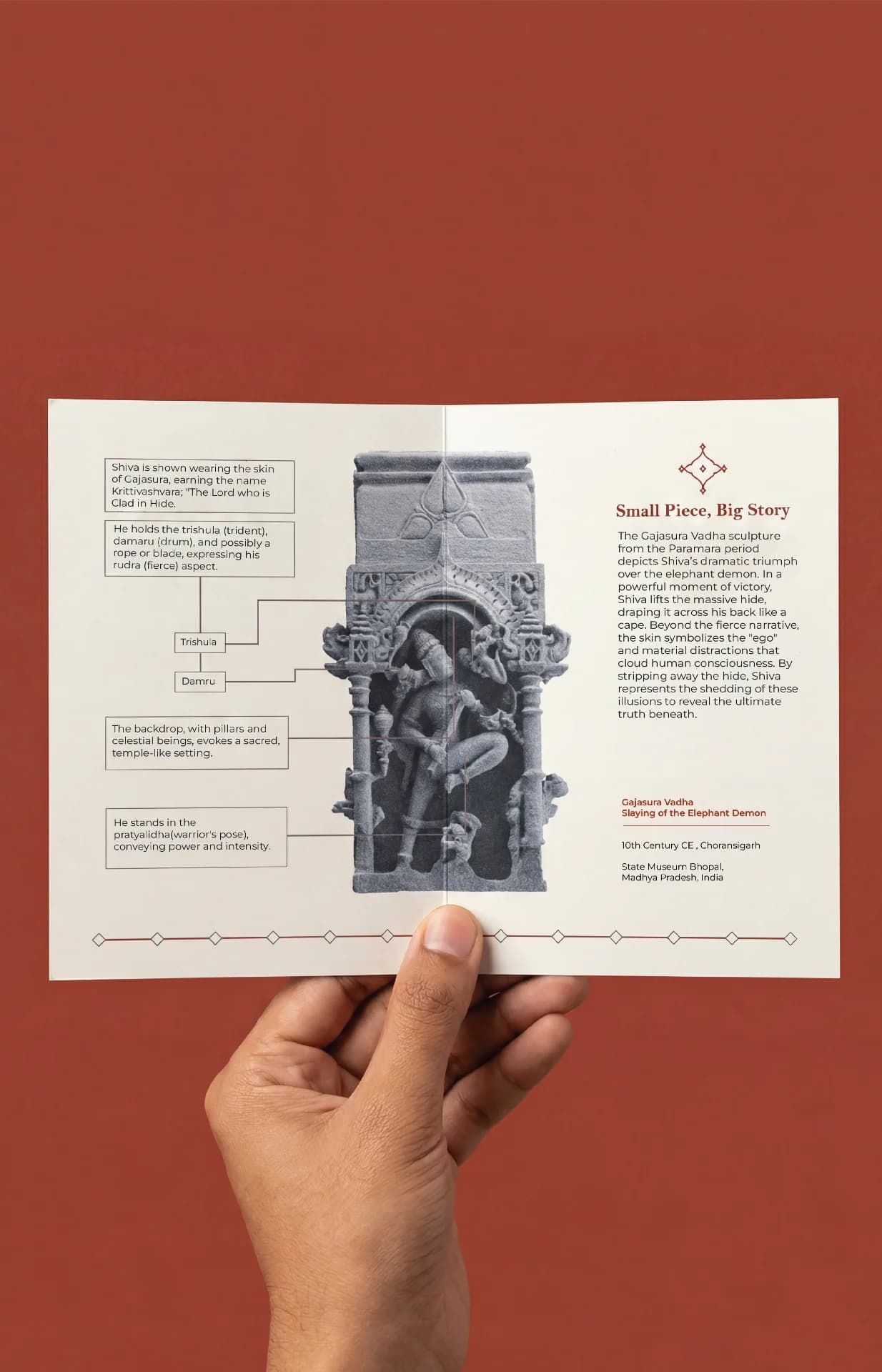A hand holds a brochure featuring the Gajasura Vadha Sculpture, displaying detailed stone-carved iconography and historical context for the museum replica.