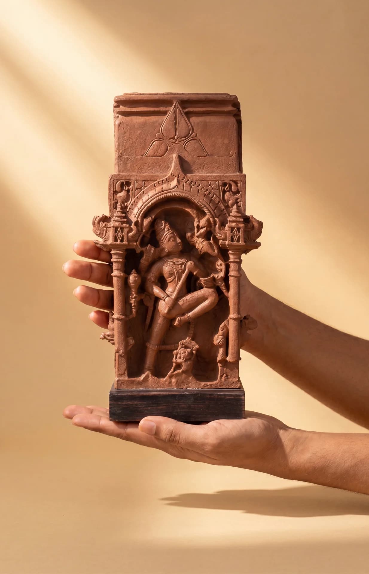 Hands hold a Gajasura Vadha Sculpture, a terracotta-style museum replica featuring intricate temple relief carvings of Shiva.