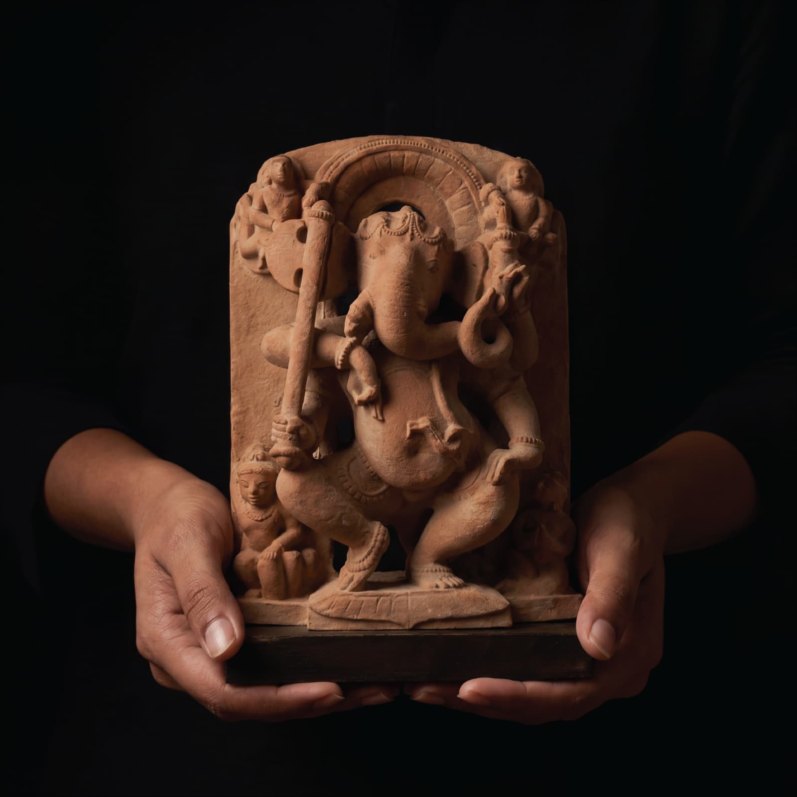 A pair of hands holds a handcrafted sandstone Ganesha Sculpture, showcasing the intricate 10th-century temple art replica details.