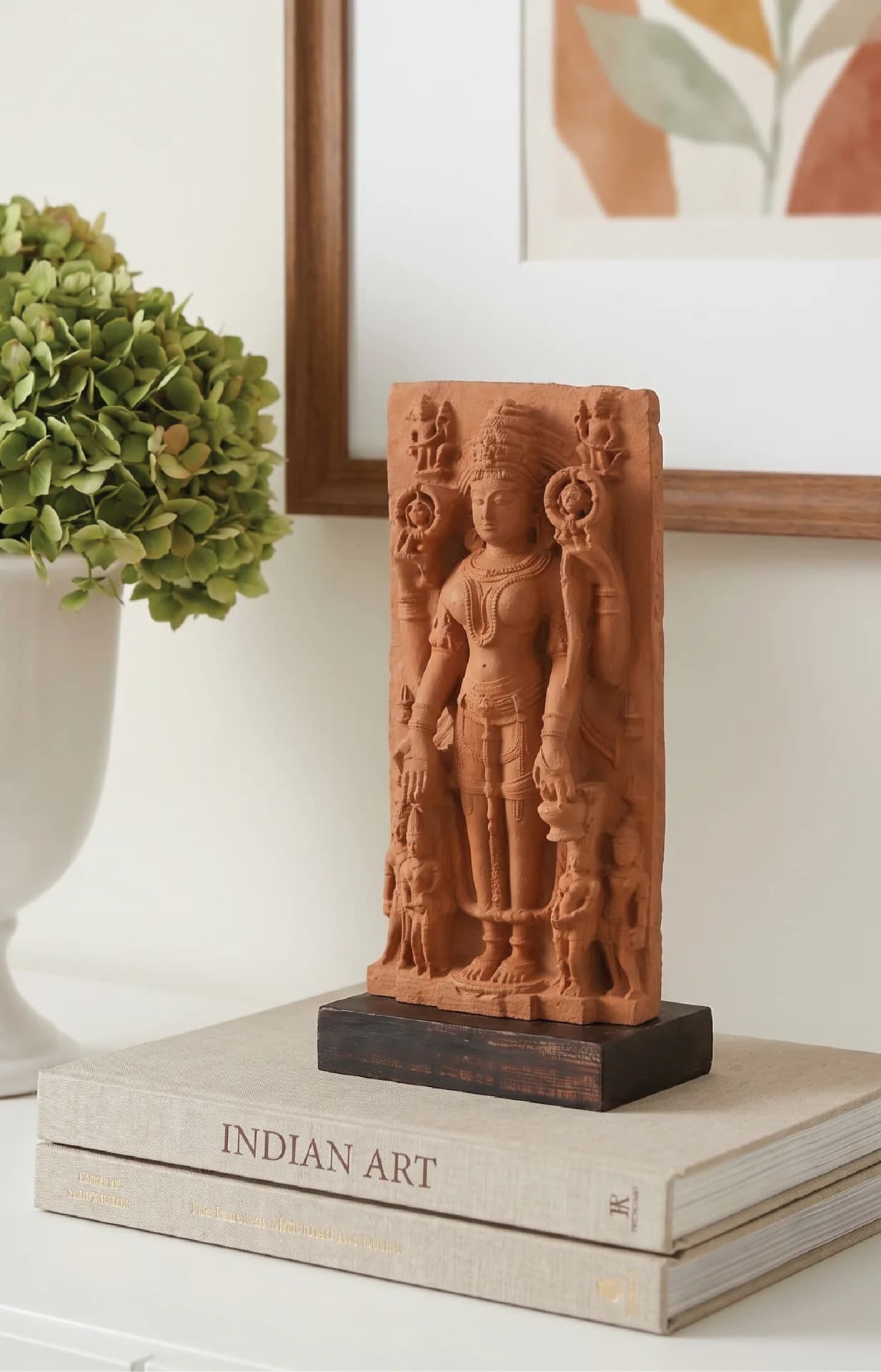 A Gauri Parvati Sculpture museum replica in stone composite displayed on a stack of books with greenery nearby.