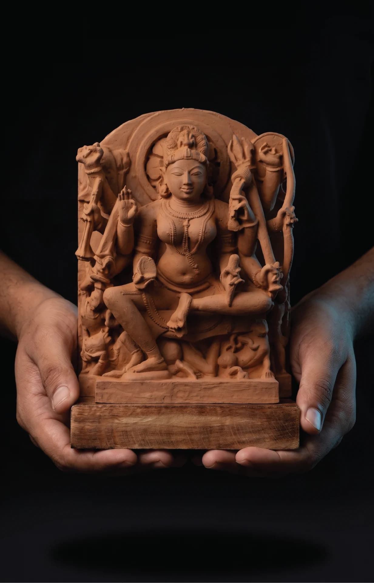 A pair of hands holds a hand-finished stone Goddess Durga Sculpture, showcasing the intricate medieval-style carved relief detail.