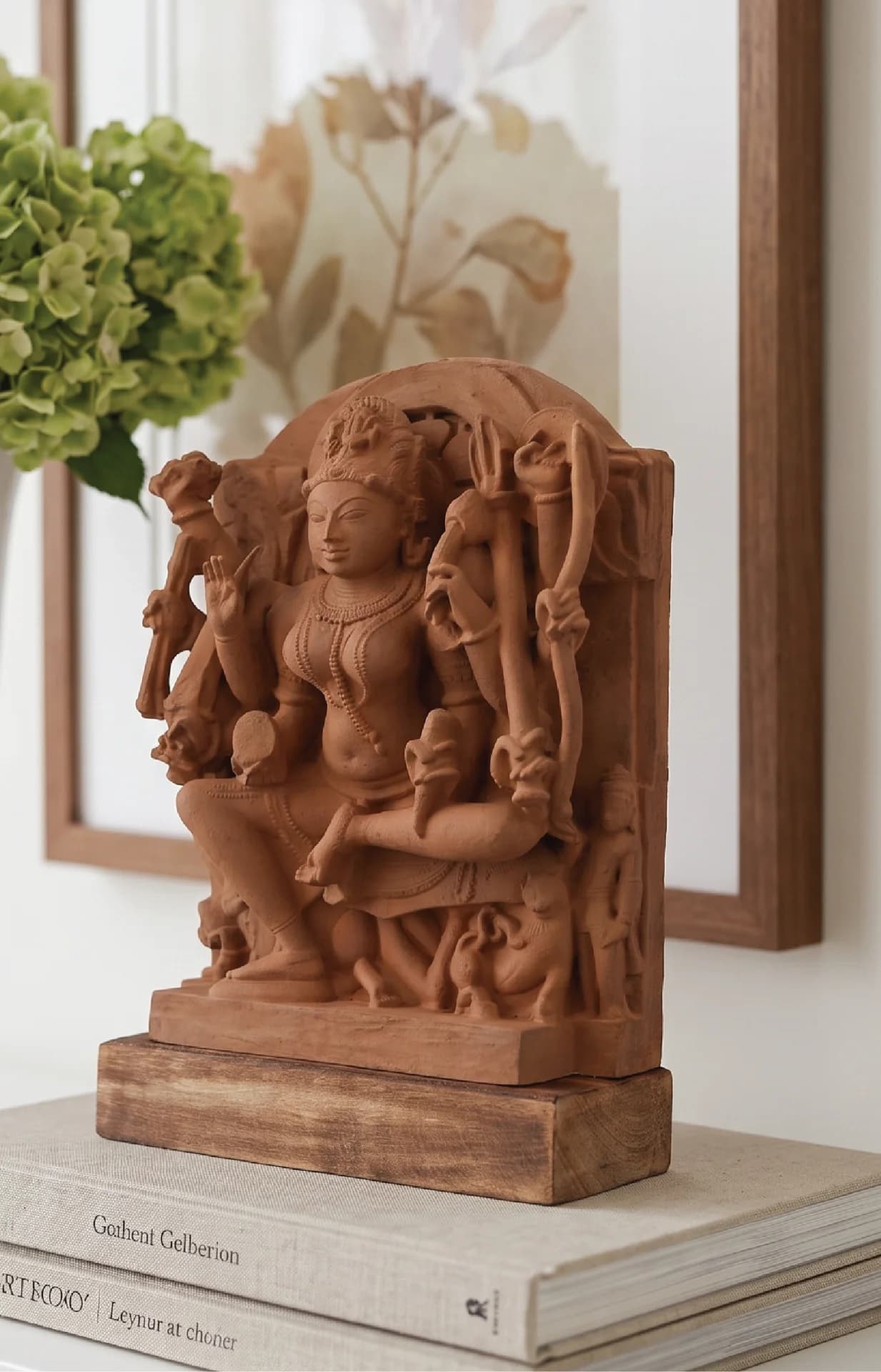 A hand-finished stone Goddess Durga Sculpture displayed on a book, featuring intricate medieval carvings of the seated deity.