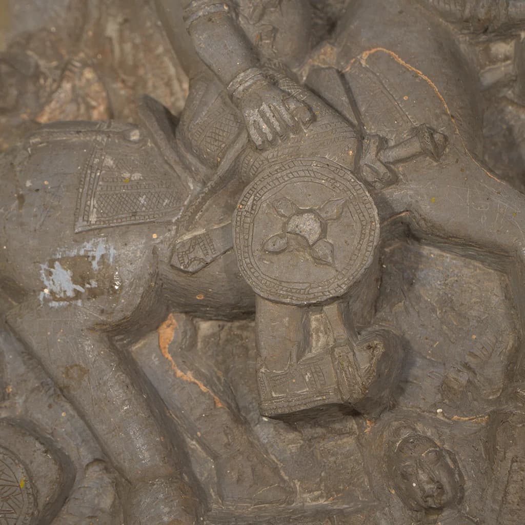 A detailed closeup of the Goud Yoddha Sculpture showing the stone-carved shield and horseman's hand in a traditional relief style.