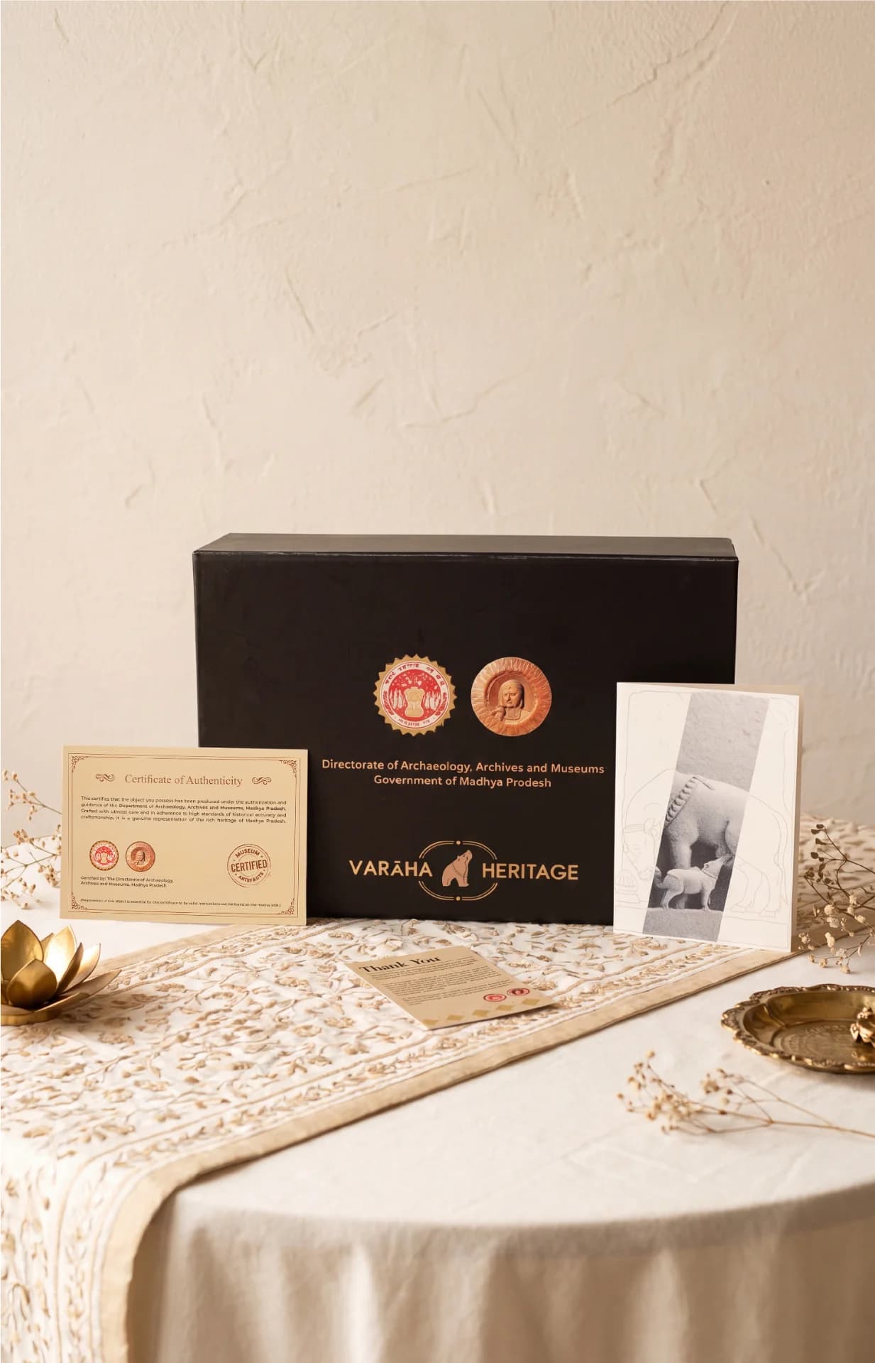 The Kamdhenu Sculpture packaging box displayed with its official certificate of authenticity and a heritage information card on a table.